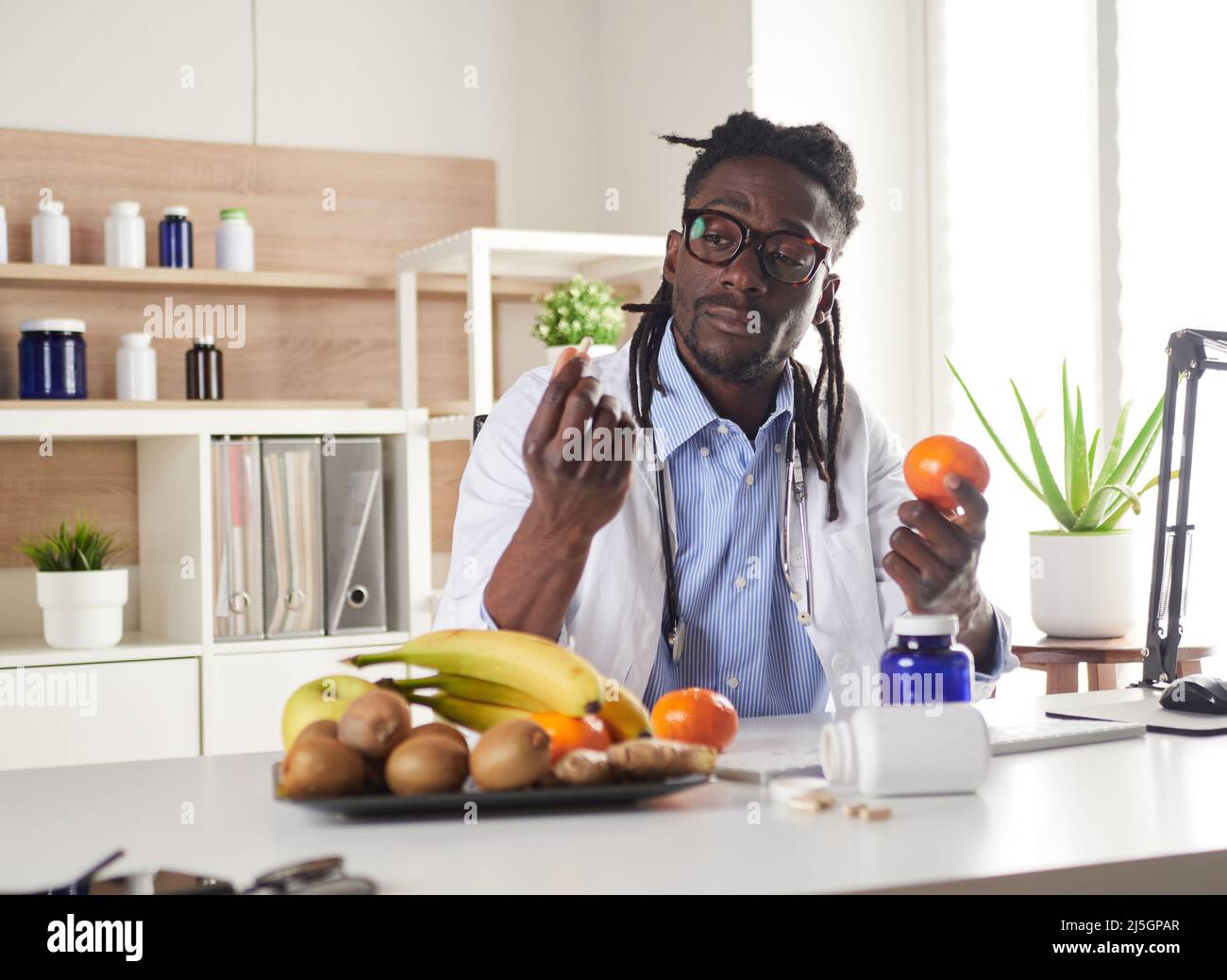 Der afroamerikanische Ernährungsberater schaut sich die Kamera an und zeigt gesunde Früchte in der Konsultation. Stockfoto