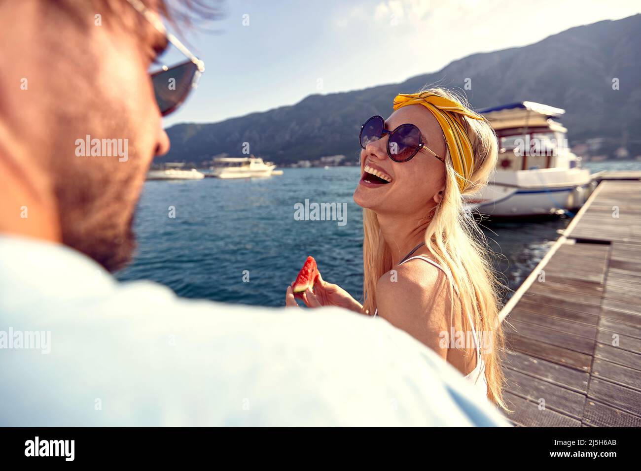 Schöne lächelnde Blondine, die Wassermelone hält und ihren männlichen Partner anschaut. Zweisamkeit, Lifestyle, Luxuskonzept. Stockfoto