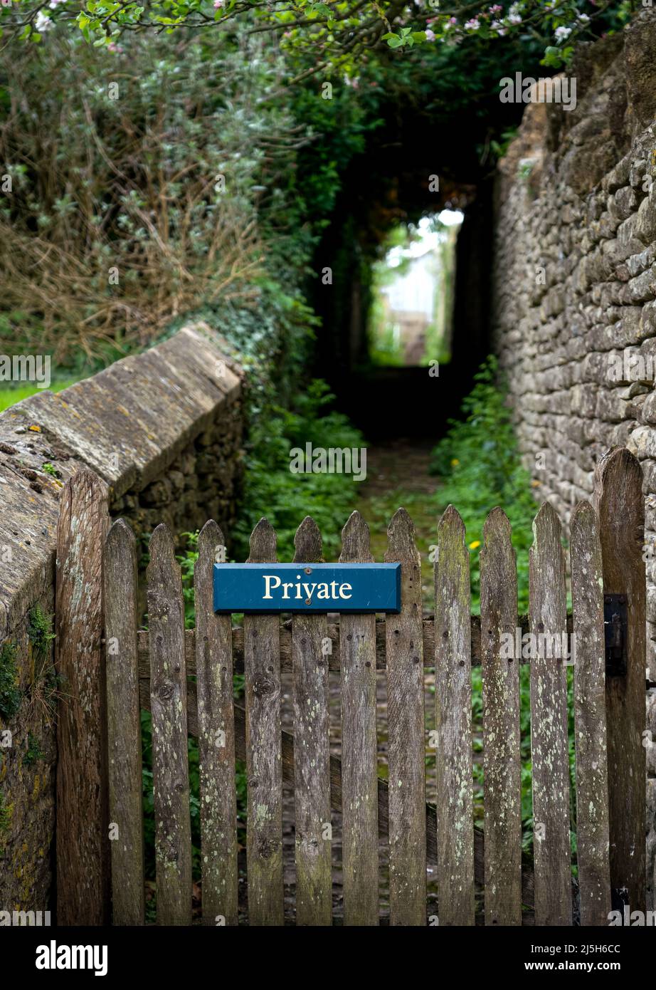 Holztor mit weißem Text auf blauem Hintergrund privates Schild, das zu einem Pfad unter Laub führt, unfokussierter Hintergrund Stockfoto