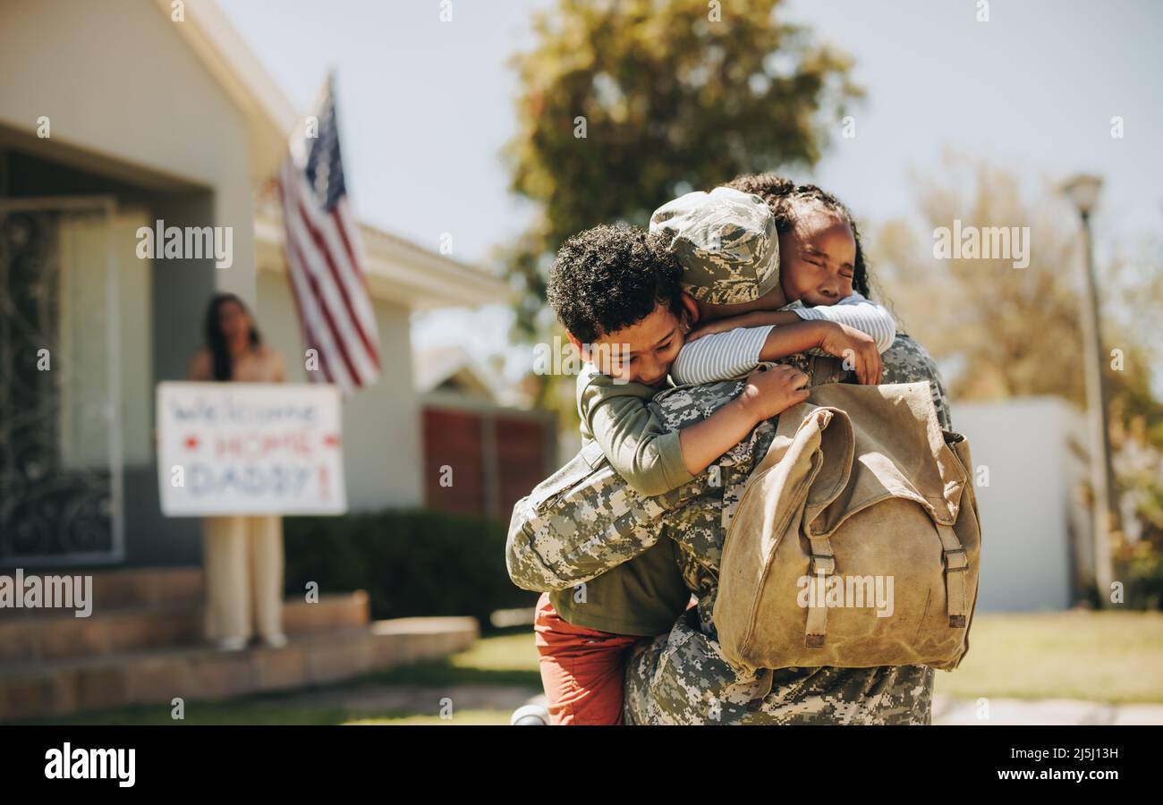 Emotionales Familientreffen. Militärvater umarmte seine Kinder, nachdem er von der Armee nach Hause zurückgekehrt war. Amerikanischer Soldat, der von seinem Freund herzlich empfangen wurde Stockfoto