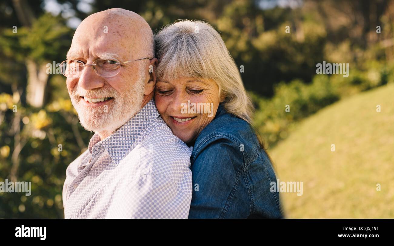 Glückliches reifes Paar umarmt sich gegenseitig, während sie in einem Park stehen. Romantisches, älteres Paar, das lächelt und gemeinsam die Sonne genießt. Liebevoller Senior Stockfoto