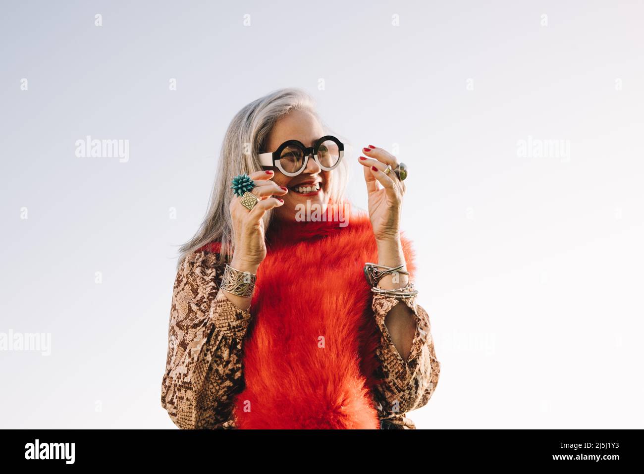 Glückliche reife Frau lächelt fröhlich, während sie im Freien steht. Glückselige ältere Frau in farbenfroher Freizeitkleidung im Sommer. Sorglos reif Stockfoto