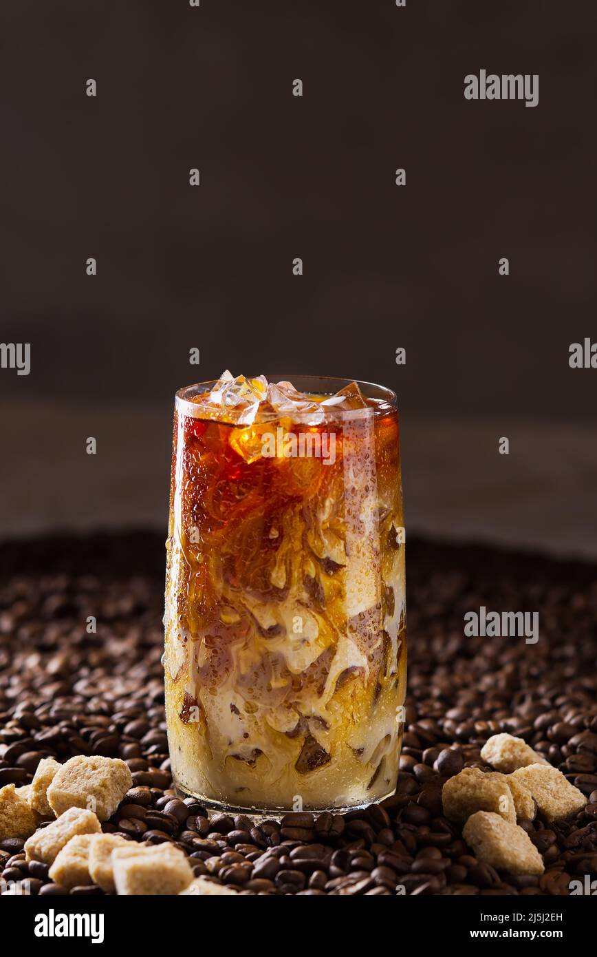 Eiskaffee. Leckerer Eiskaffee mit Milch, kaltes Getränk im Glas mit Eis auf dunklem Kaffeehintergrund. Stockfoto