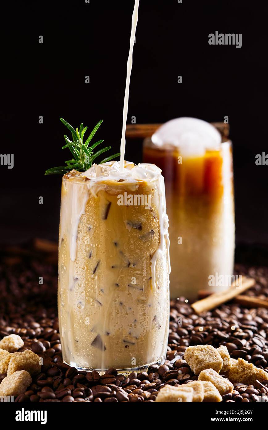 Eiskaffee. Leckerer Eiskaffee mit Milch, kaltes Getränk im Glas mit Eis auf dunklem Kaffeehintergrund. Stockfoto