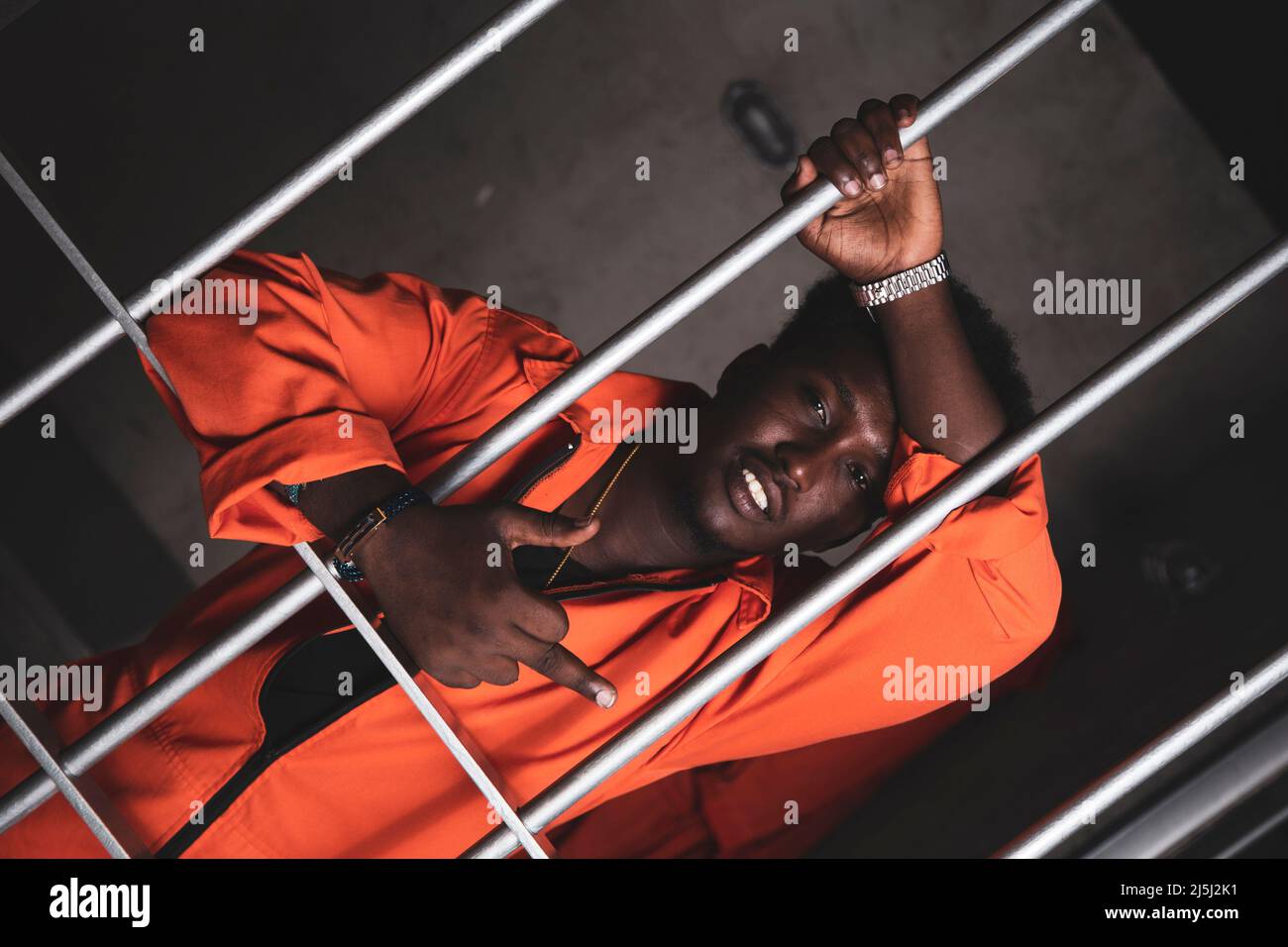 Schwarzer Gefangener in einem orangefarbenen Jumpsuit, der seinen Zellenzaun lehnt. Stockfoto