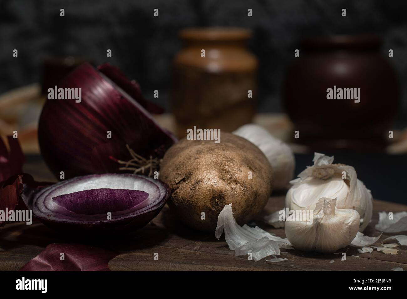 Rohe Kartoffel mit Zwiebel und Knoblauch in dunkler Stimmung. Stockfoto