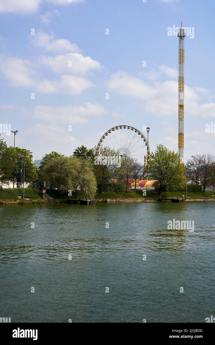Stuttgart, Deutschland - 22. April 2022: Frühlingsfest mit lustigen Fahrgeschäften. Riesenrad und Freifallturm am Fluss am Mittag. Deutschland, Stockfoto