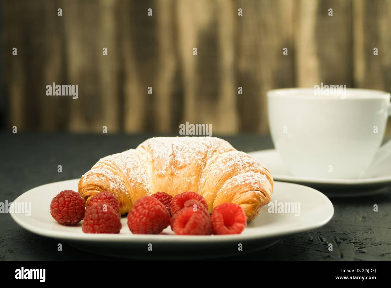 Croissants und frische Himbeeren, frische und leckere Croissants. Frühstück im Hotel: Kaffee mit Milch und Croissants, frische Himbeeren auf einem Holz Stockfoto