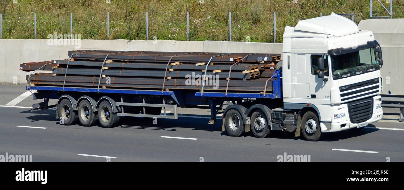 Vorder- und Seitenansicht weißer LKW-LKW-LKW-LKW-LKW DAF mit Fahrer in Zugmaschine mit flachfahrenden Sattelaufliegern, beladen mit Stahlträgern auf der britischen Autobahn Stockfoto