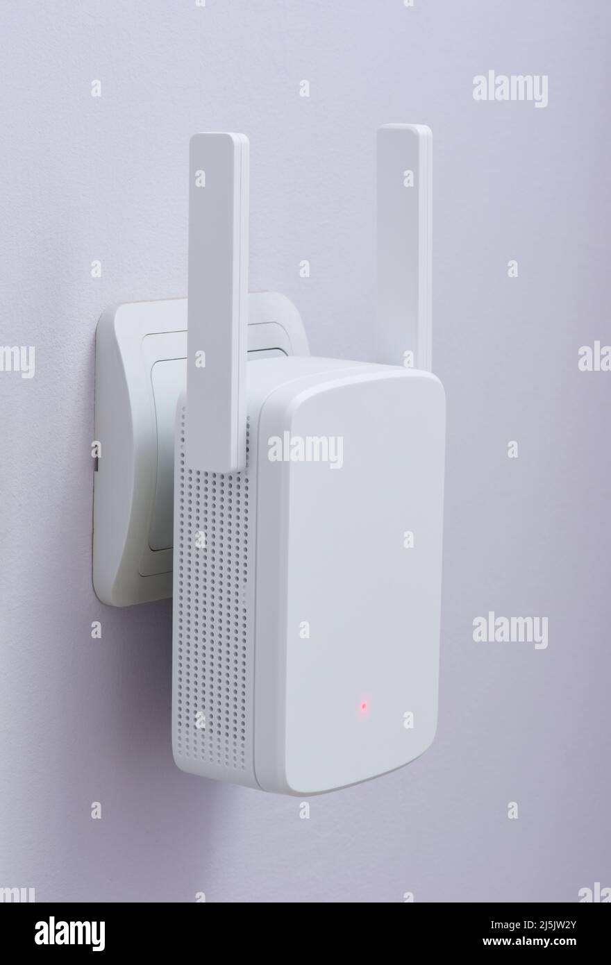 Weißer wi-Fi-Reichweiten-Extender, an der blauen Wand an eine Steckdose angeschlossen Stockfoto