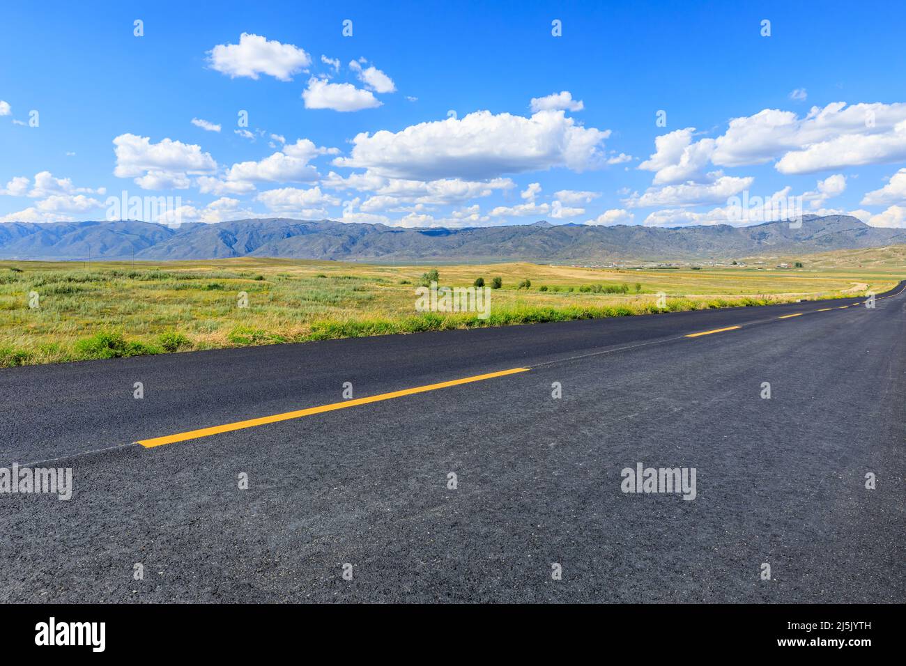Leere Asphaltstraße und grünes Grasland und Berg unter blauem Himmel in Xinjiang, China. Stockfoto