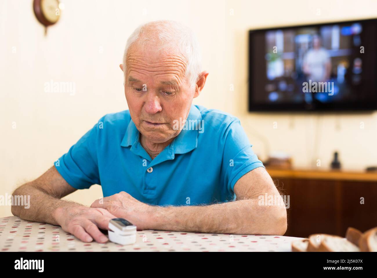 Fokussierter besorgter älterer Mann, der sich mit Hilfe des Pulsoximeters am heimischen Tisch selbst die Sauerstoffsättigung misst. Selbstkontrollkonzept für die Gesundheit Stockfoto