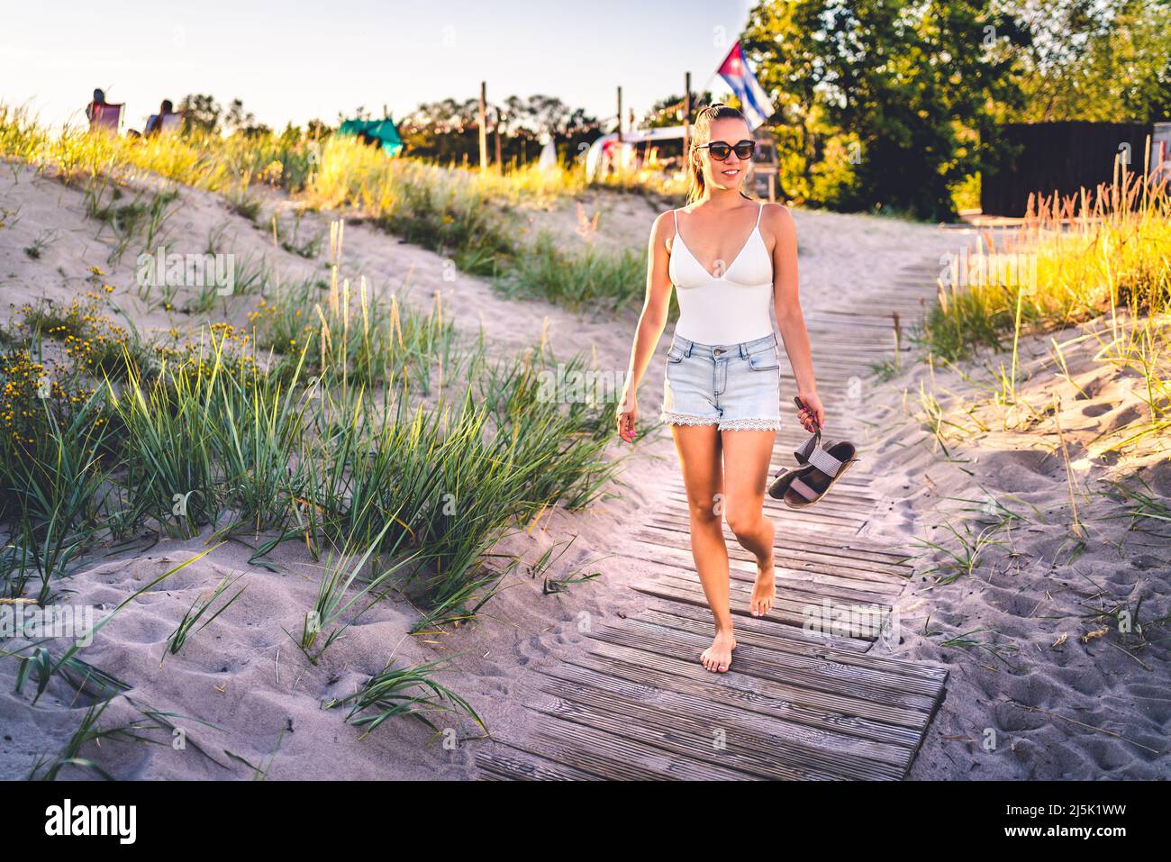 Frau, die im Sommer auf der Strandpromenade bei Sonnenuntergang spazierengeht. Outdoor Natur Porträt von glücklich hübsches Mädchen genießen das Leben und sommerliche Vibes. Stockfoto