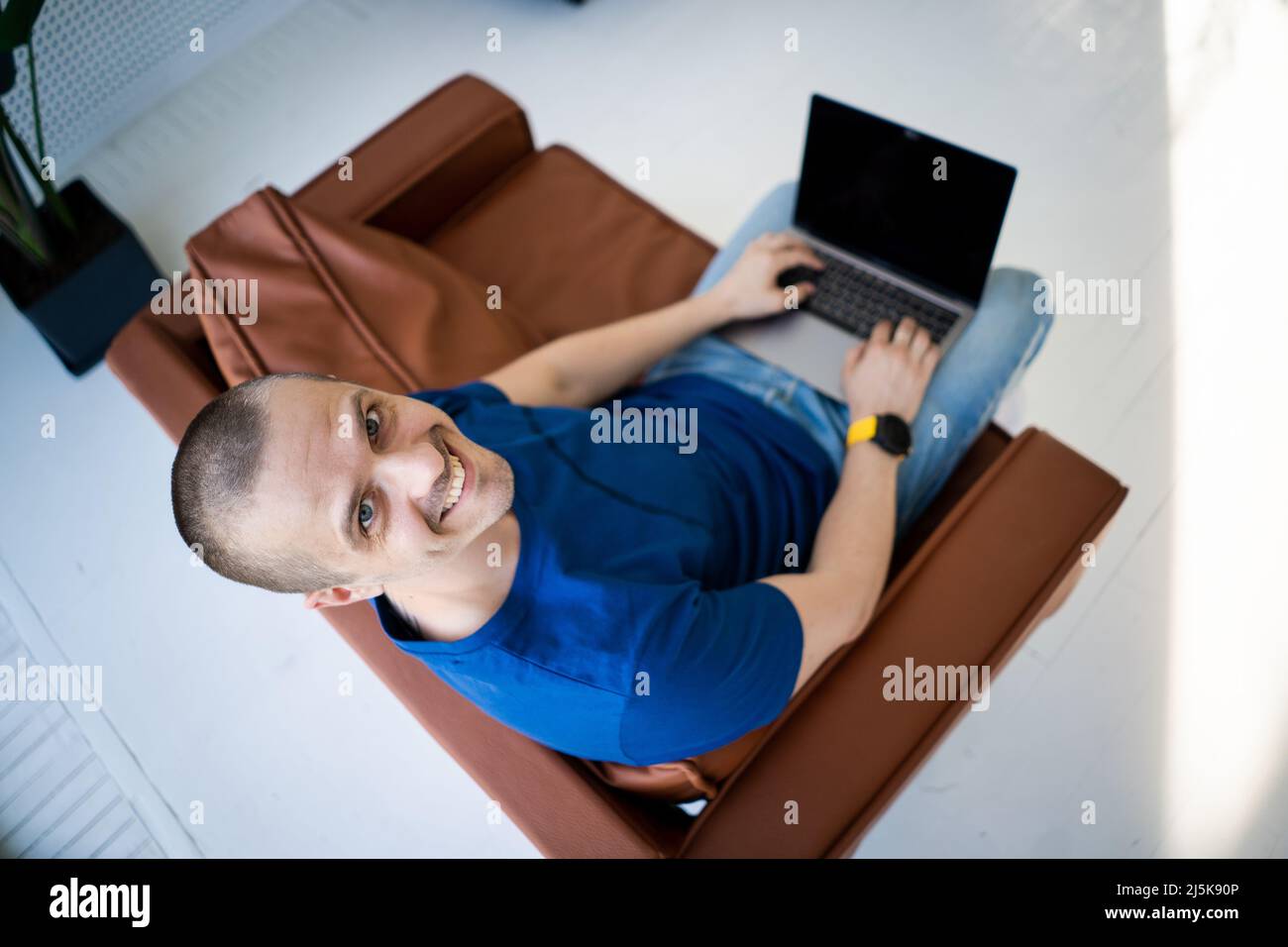 Freier Mann, der an einem Laptop arbeitet, der auf einem Stuhl sitzt Stockfoto