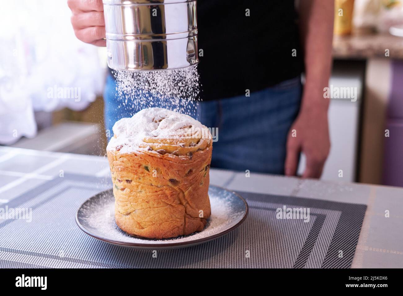 Zuckerpulver auf einen leckeren Osterkuchen auf einem Teller geben Stockfoto