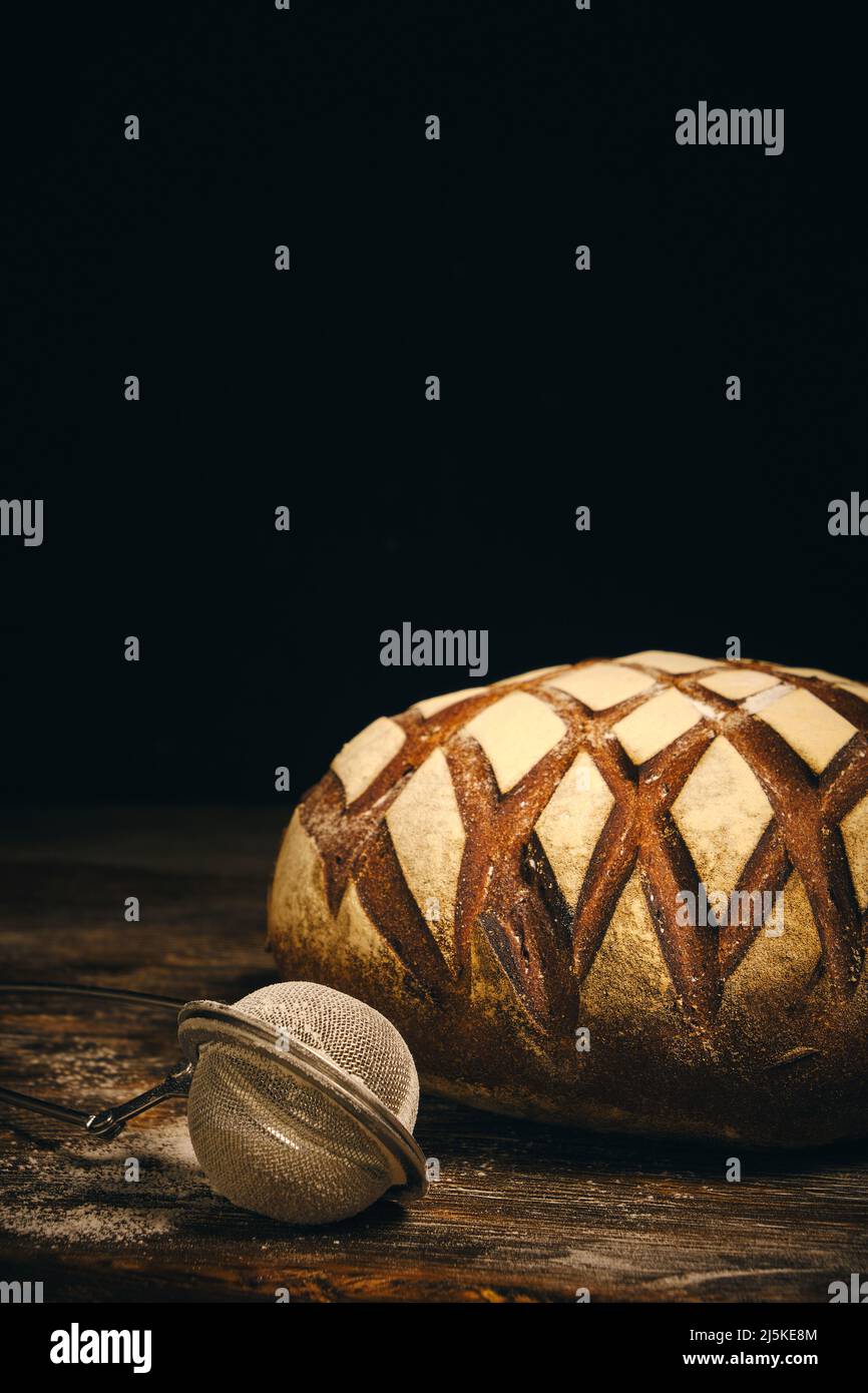 Brot aus schwarzem Roggen mit Mehl bestreut und mit Sieb auf dunklem Grund bestreuen Stockfoto