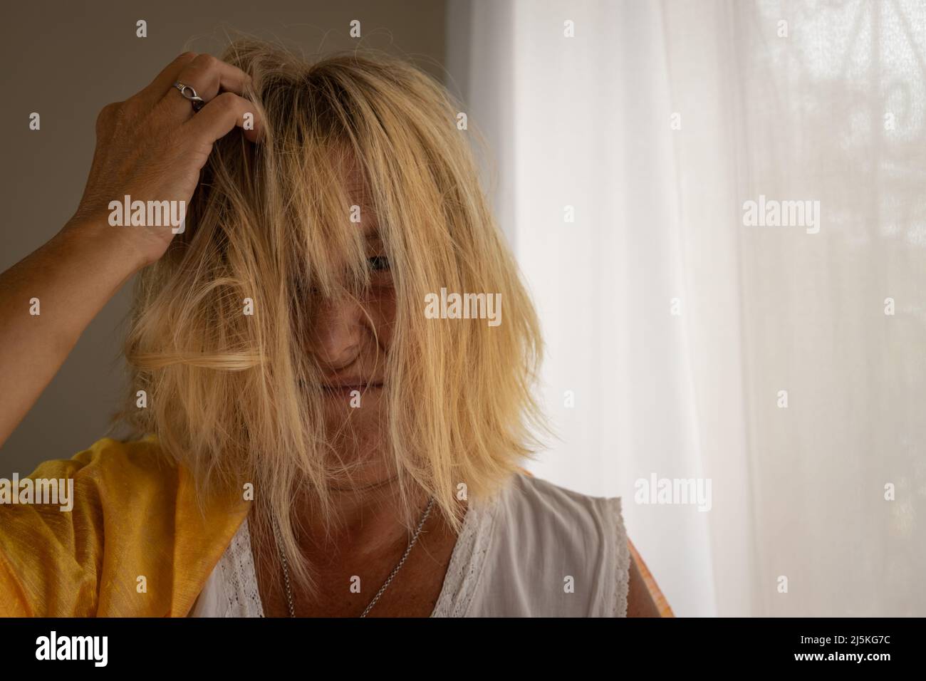 Blonde kaukasische Frau 50-60 Jahre alt mit zerzausten Haaren auf neutralem Hintergrund. Gestresstes Frauenkonzept. Stockfoto