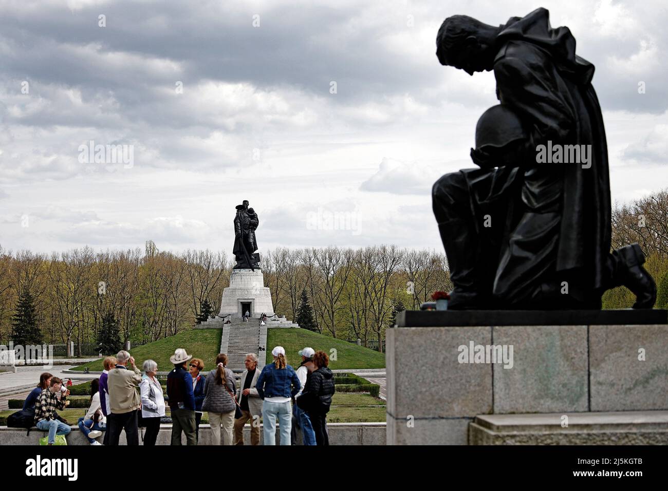 Berlin, Deutschland. 24. April 2022. Auf dem Gelände des Sowjetischen Denkmals im Treptow Park laufen Touristen an der Statue eines kniender Soldaten vorbei. Seit dem russischen Angriff auf die Ukraine gab es immer mehr Inschriften mit politischem Inhalt, die von unbekannten Personen dort platziert wurden. Quelle: Carsten Koall/dpa/Alamy Live News Stockfoto