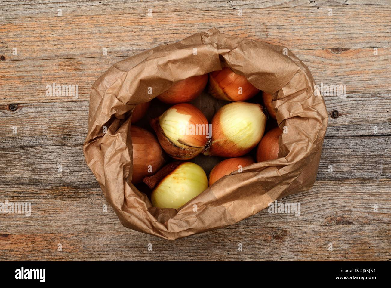 Zwiebelzwiebeln in einem Kraftpapier-Beutel auf einem Holztisch Stockfoto