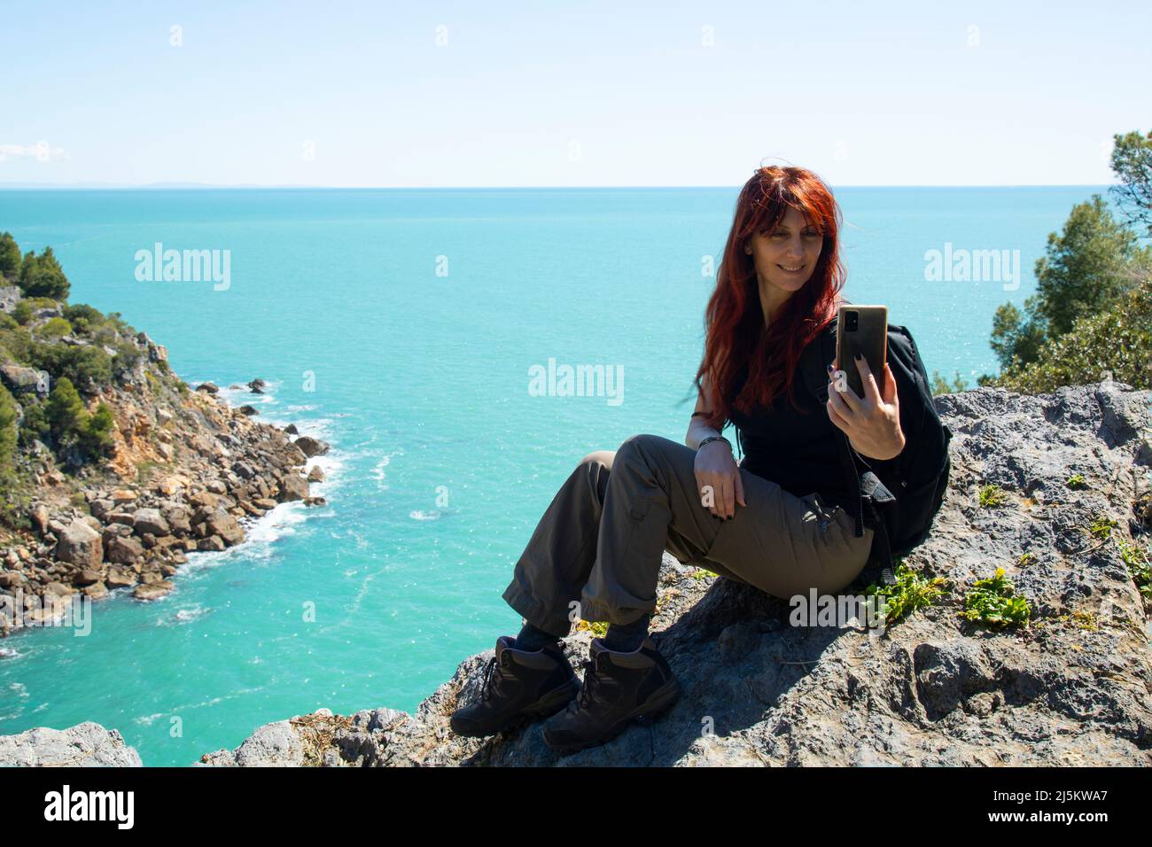 Eine Trekkingfrau auf dem Gipfel des Berges über dem Meer macht ein Selfie mit einem Mobiltelefon Stockfoto