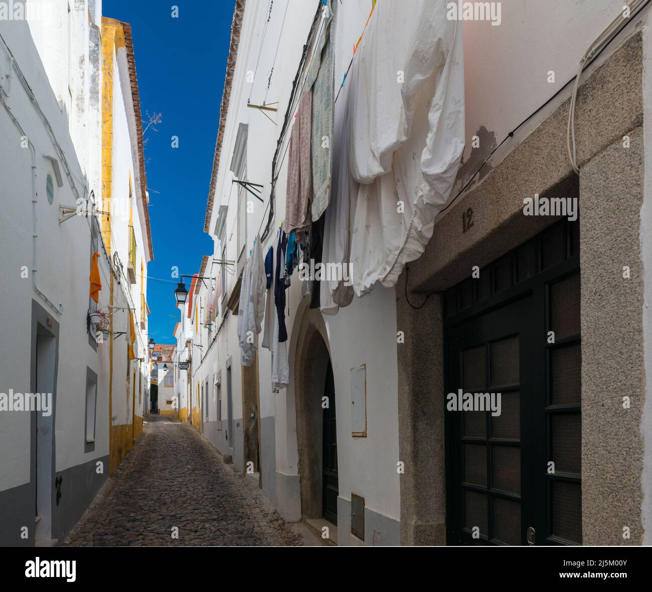 Trocknen von Wäsche in einer der malerischen Gassen mit Kopfsteinpflaster und weiß getünchten und gelben Häusern im historischen Zentrum von Evora, Portugal. Stockfoto