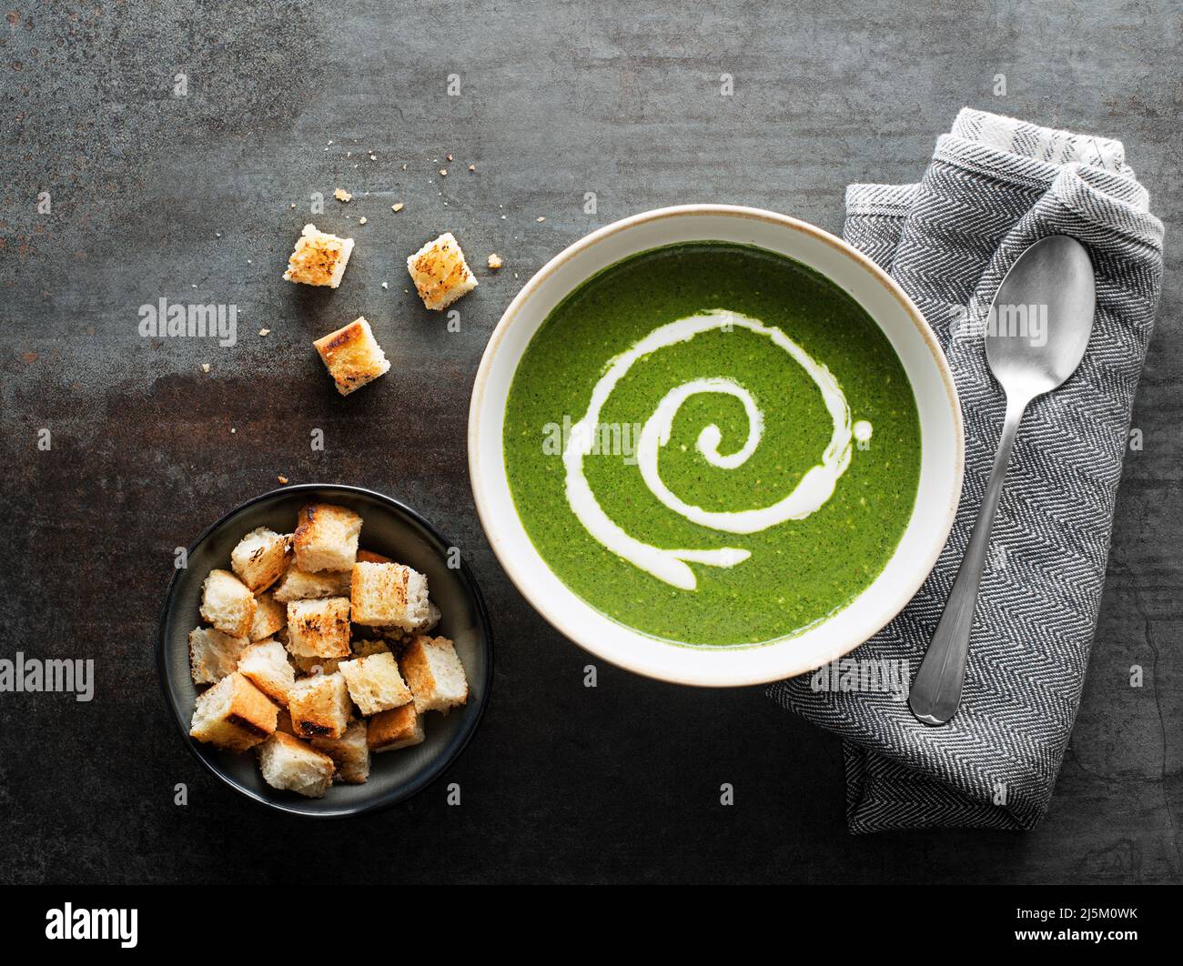 Frische grüne Suppe mit Creme und Croutons auf grauem Hintergrund über dem Schuss. Stockfoto