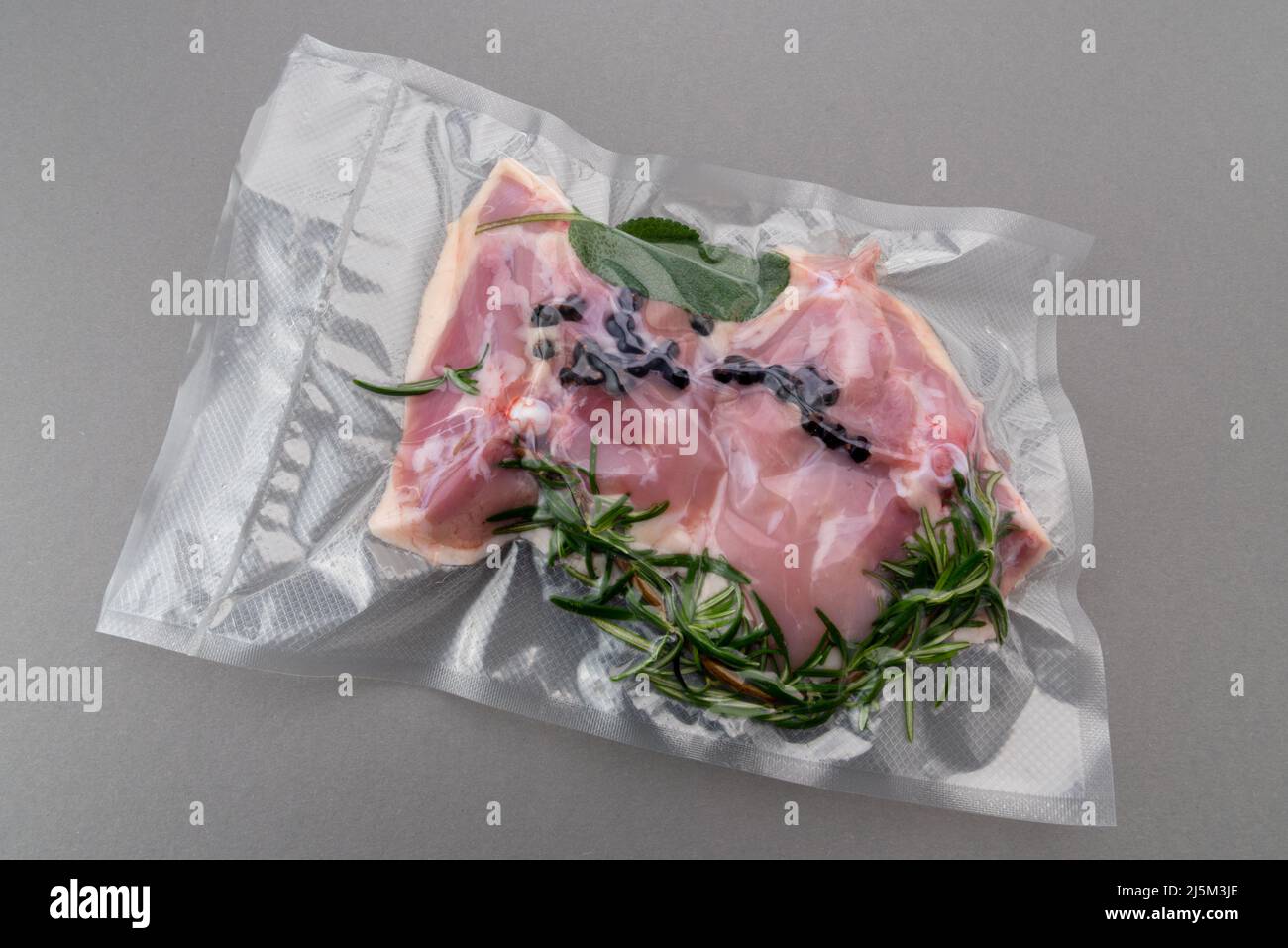 Hähnchenschenkel mit Rosmarin-Salbei und Gewürzen in vakuumverpackter Verpackung, abgedichtet für Sous-Vide-Kochen isoliert auf grauem Hintergrund in der Draufsicht Stockfoto