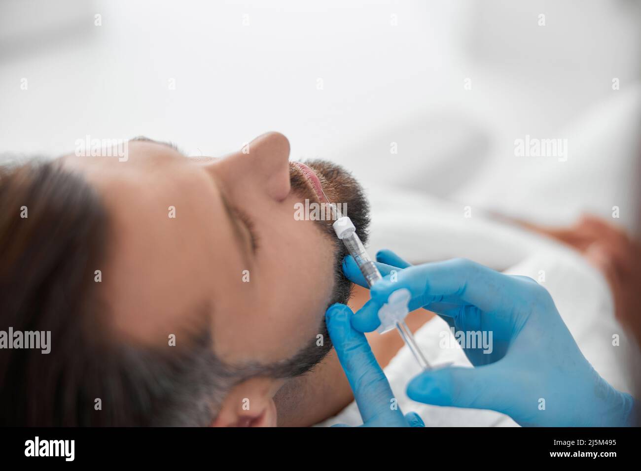 Ein hübscher Mann erfährt eine Lippenvergrößerung mit einer professionellen Kosmetikerin, die in der Klinik eine Füllstoffinjektion macht Stockfoto