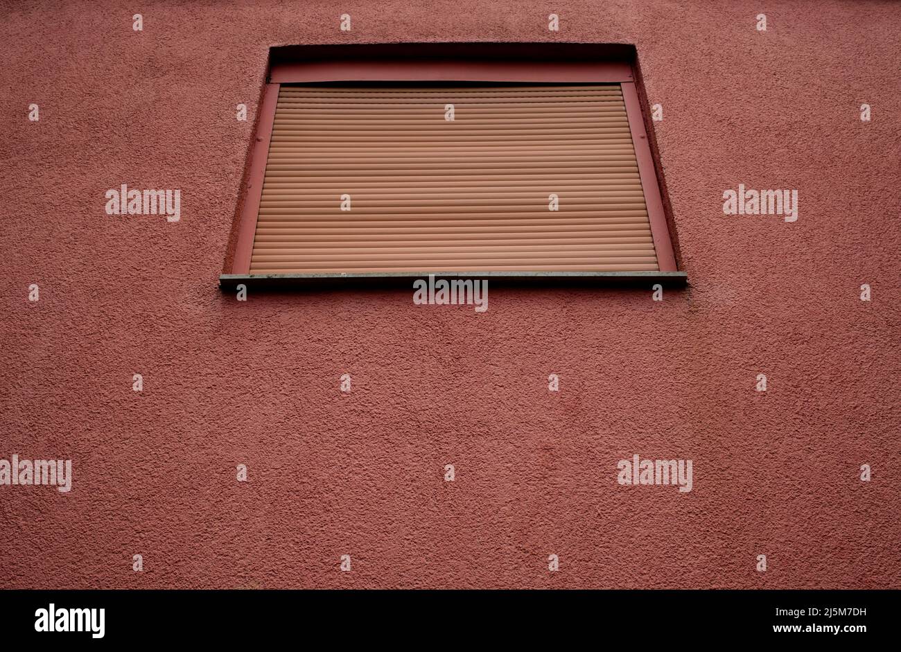Ausschnitt einer monochromen Fassade eines Gebäudes in antikem Pink mit einem einzigen Fenster mit geschlossenem Rollladen, Freiraum Stockfoto
