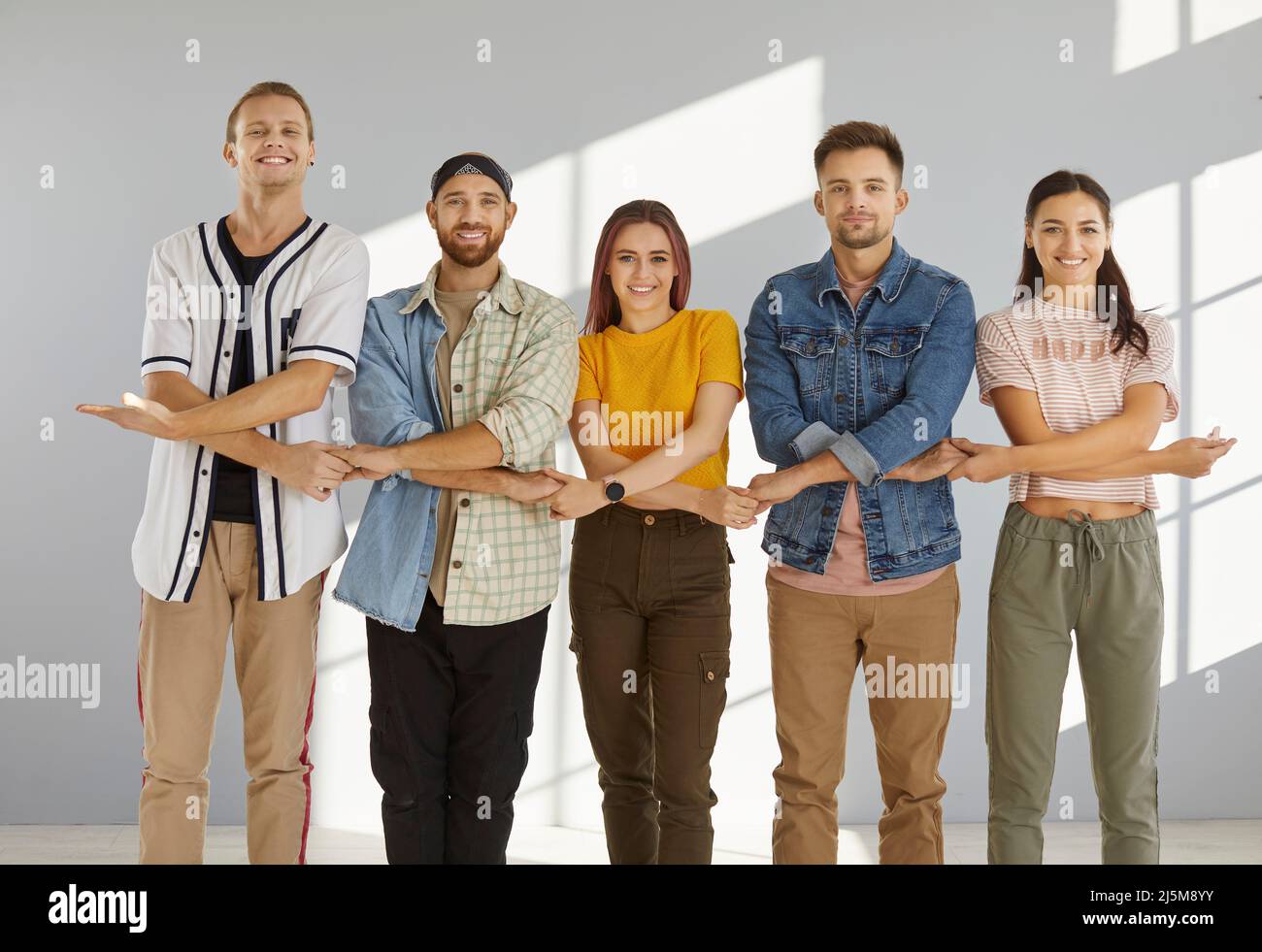 Ein Team glücklicher, fröhlicher junger Menschen, die zusammen stehen, die Hände halten und lächeln Stockfoto