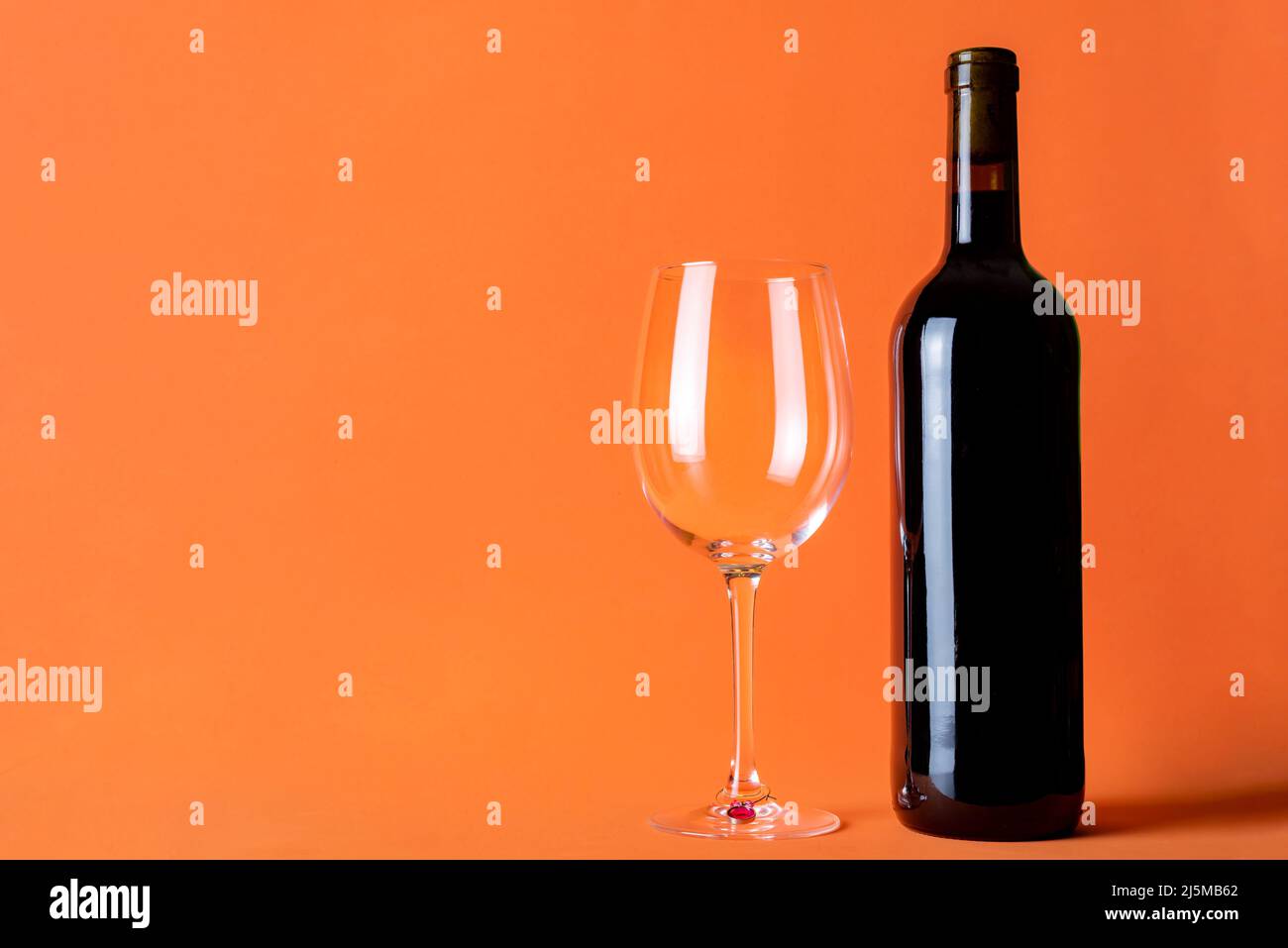 Eine Flasche Rotwein neben einem leeren Glas auf einem orangefarbenen Hintergrund. Stockfoto