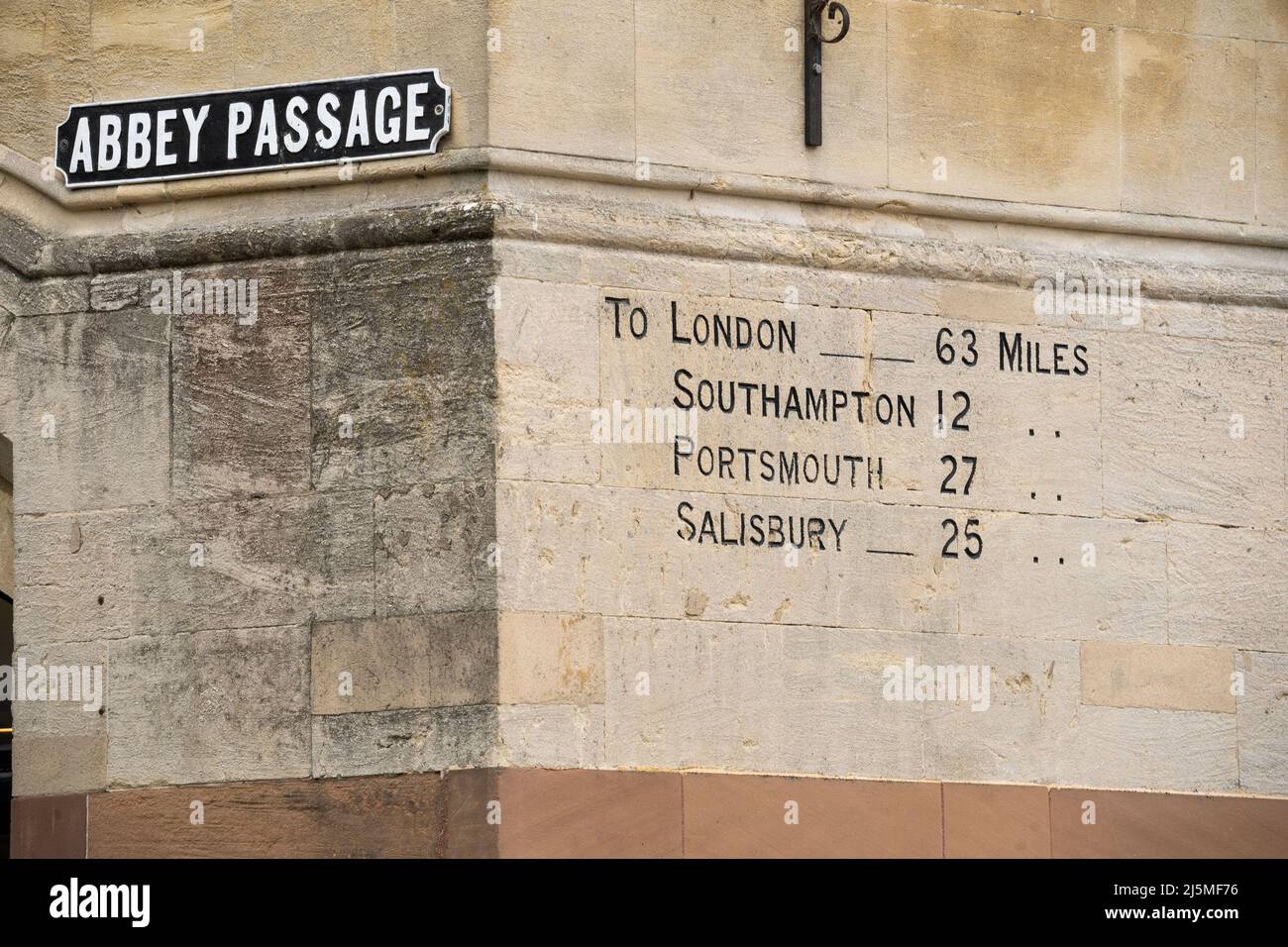 Meilensteinmarkierung mit Entfernungen zu verschiedenen englischen Städten und einem Abbey Passage Straßenschild an der Seite des viktorianischen Guildhall Winchester Stockfoto