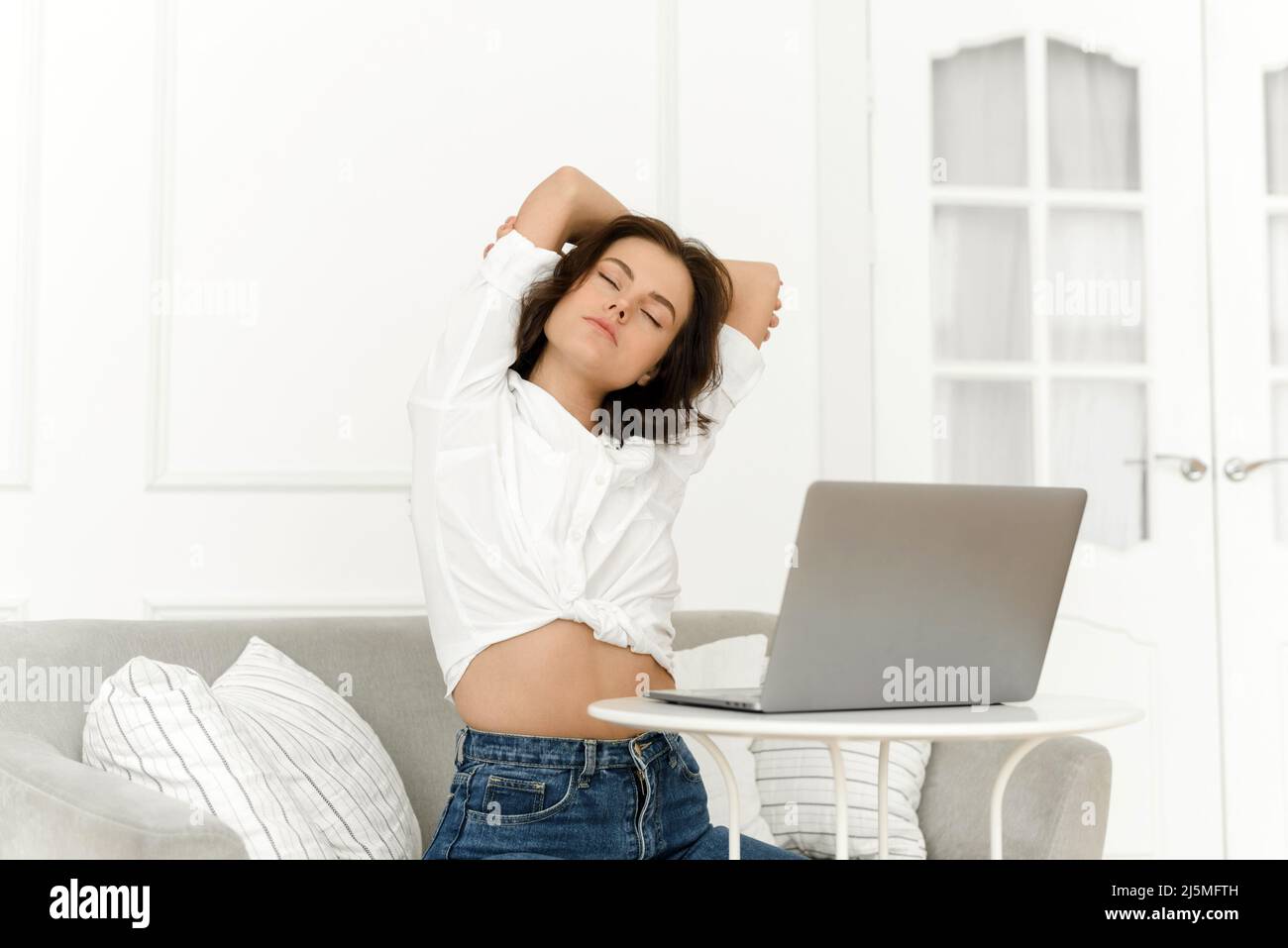 Müde Geschäftsfrau mit Rückenschmerzen, während sie zu Hause auf einem Laptop arbeitet. Junge Frau zufrieden mit dem Abschluss der Arbeit am Computer stret Stockfoto