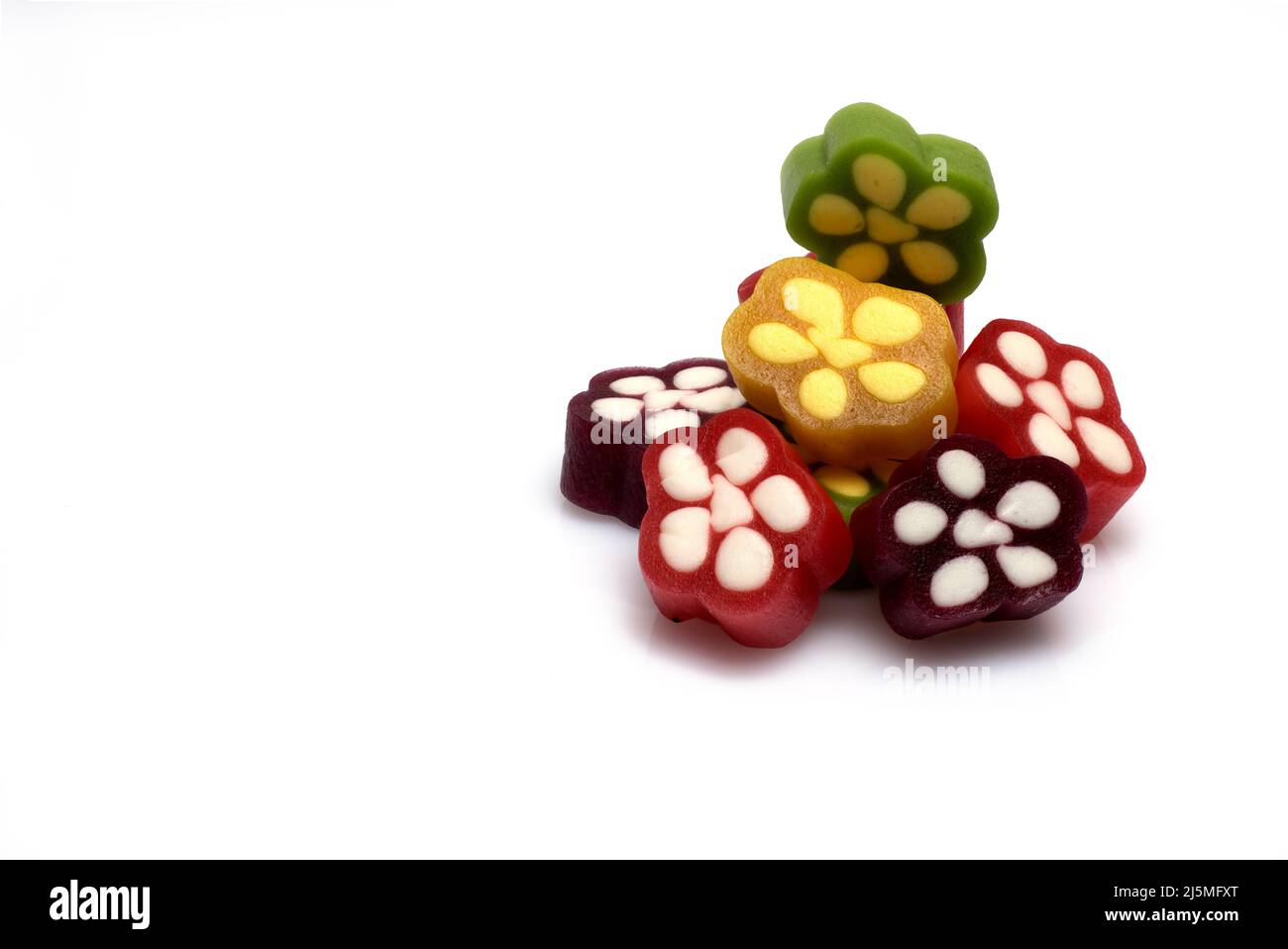 Nahaufnahme von bunten, rot-gelb-grünen Gummibonbons, übereinander gestapelt und nebeneinander in Blütenform mit weißen Punkten auf weißem Hintergrund Stockfoto