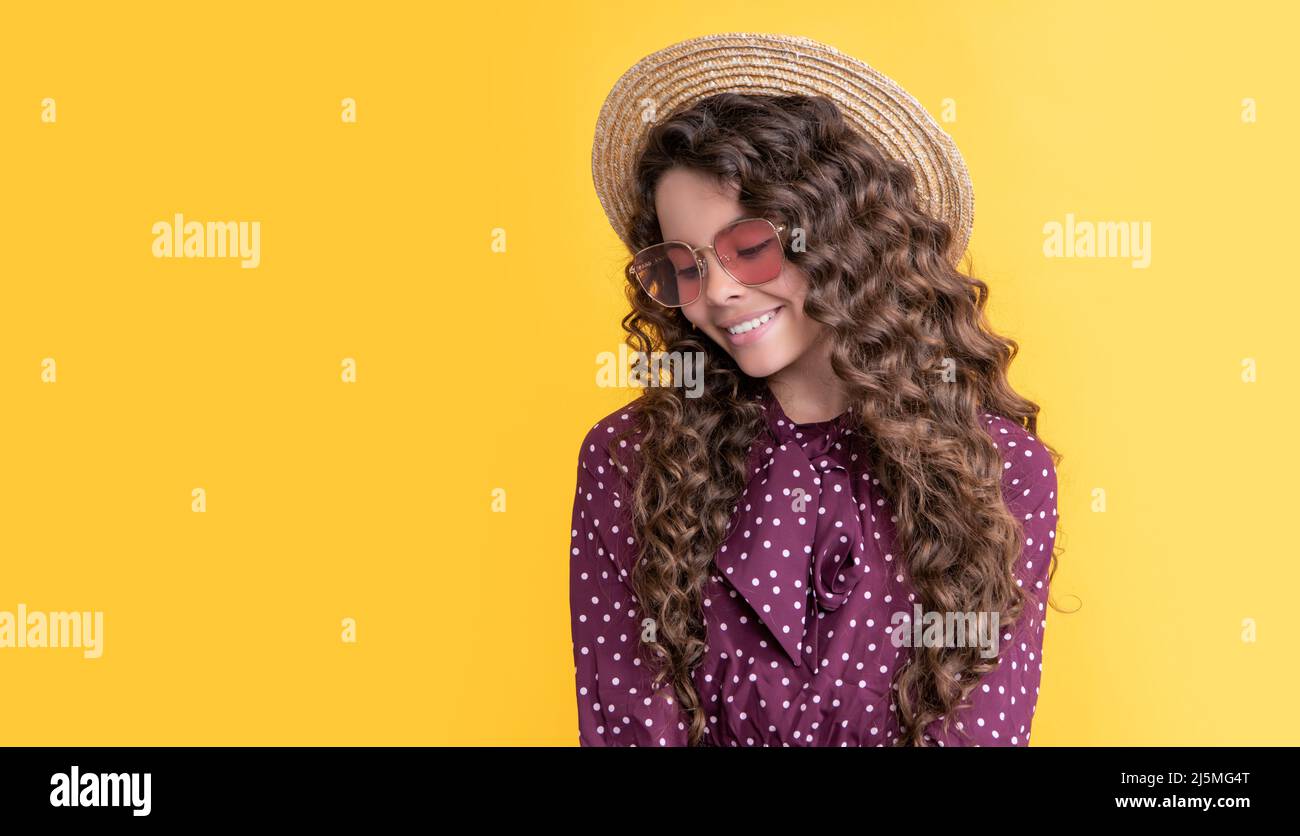 Fröhliches Mädchen in Strohhut und Sonnenbrille mit langen Brünette lockiges Haar auf gelbem Hintergrund Stockfoto