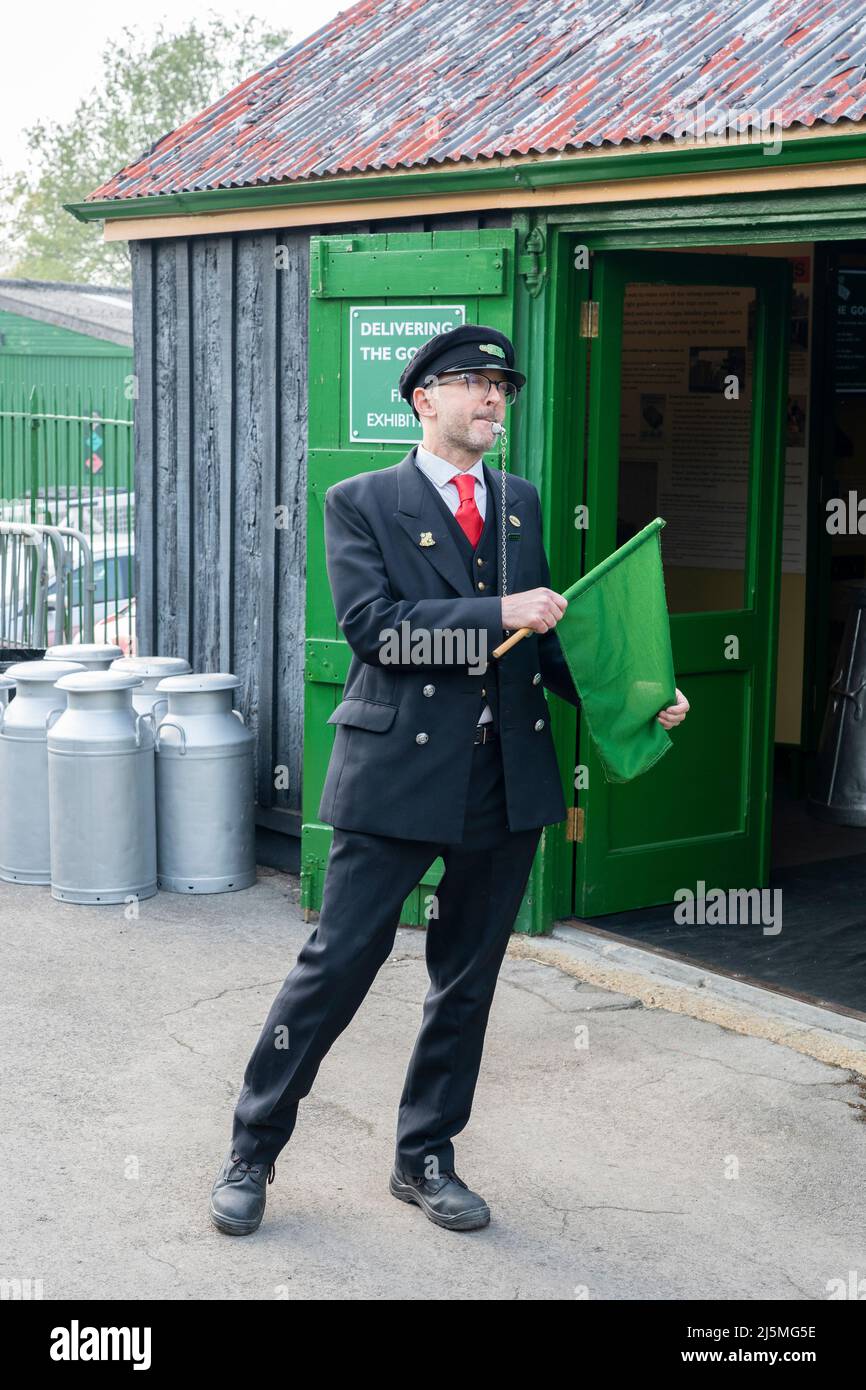 Wache in traditioneller Uniform der British Railways, pfeifend und mit grüner Flagge winkend. Watercress Railway Line, Hampshire, England Stockfoto