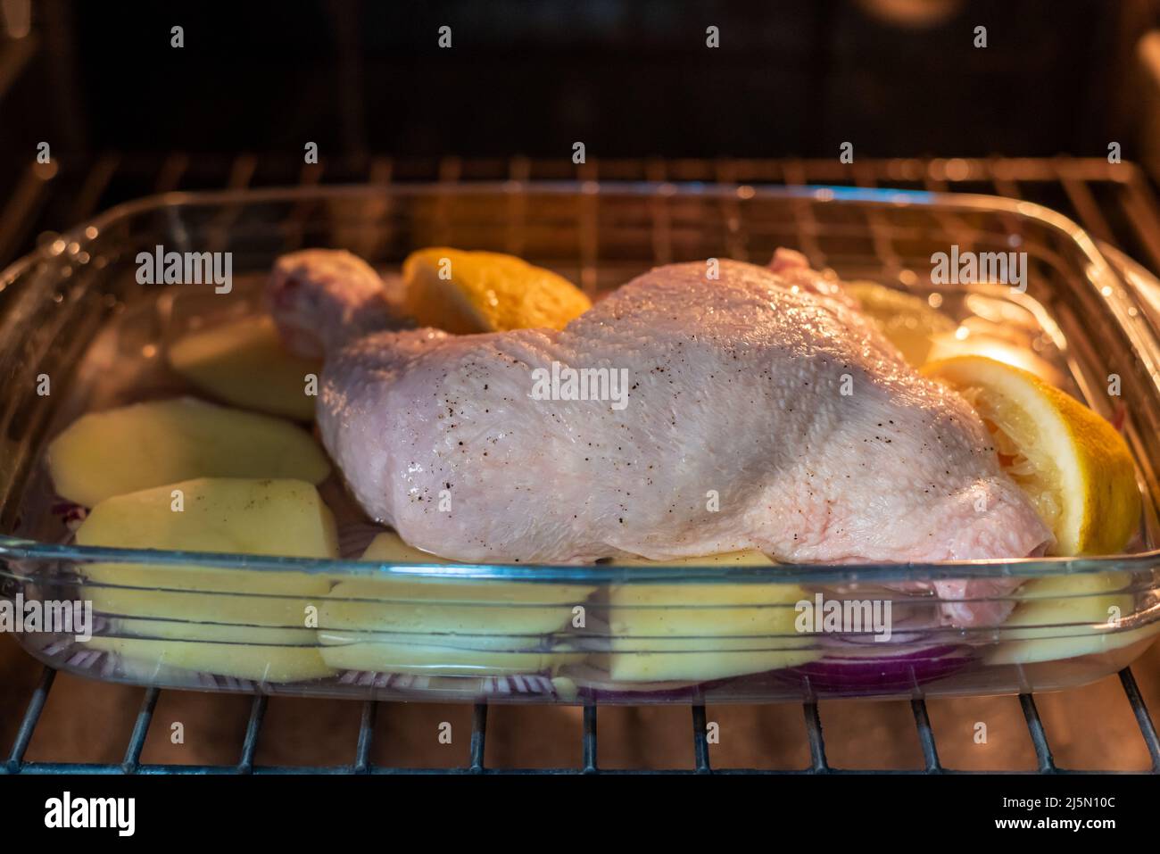 Frisch gebackenes Tablett mit Zitronenhuhnschenkel, Kartoffeln und roten Zwiebeln. Stockfoto