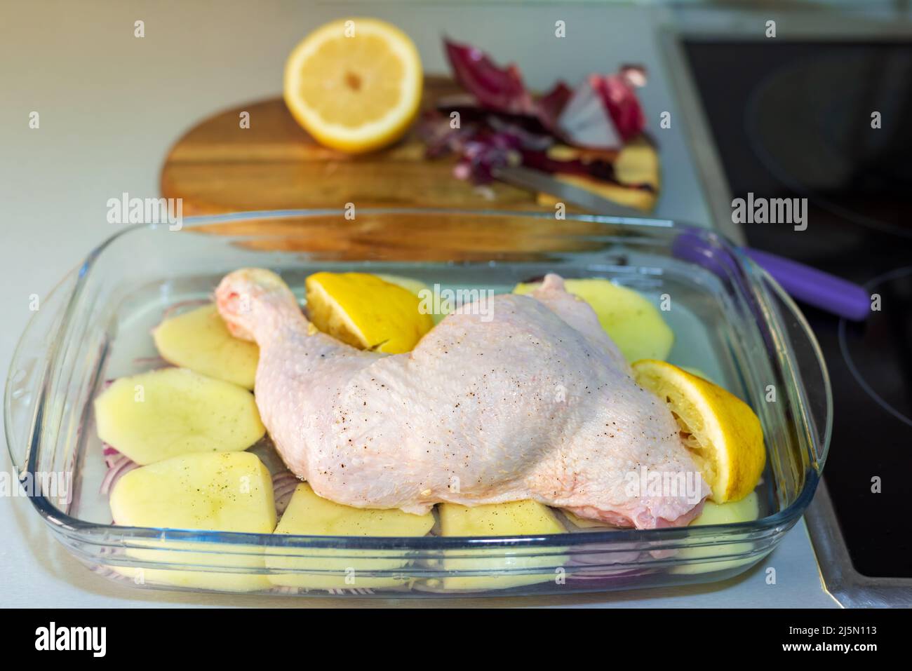 Tablett auf der Küchentheke mit Zitrone Huhn Oberschenkel, Kartoffeln und roten Zwiebeln. Stockfoto