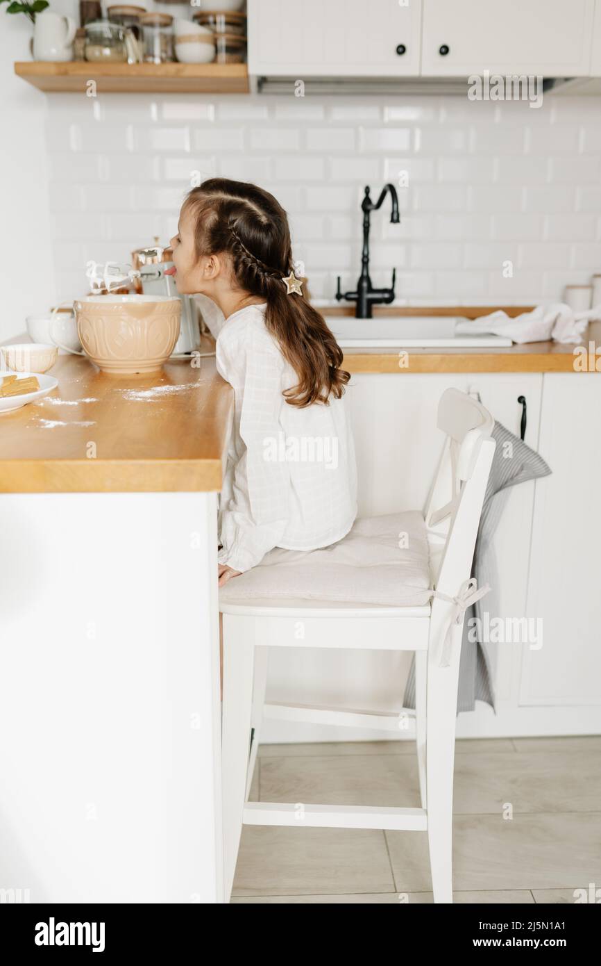 Kleines kaukasisches braunhaariges Mädchen, das zu Hause in der weißen Küche backt Stockfoto