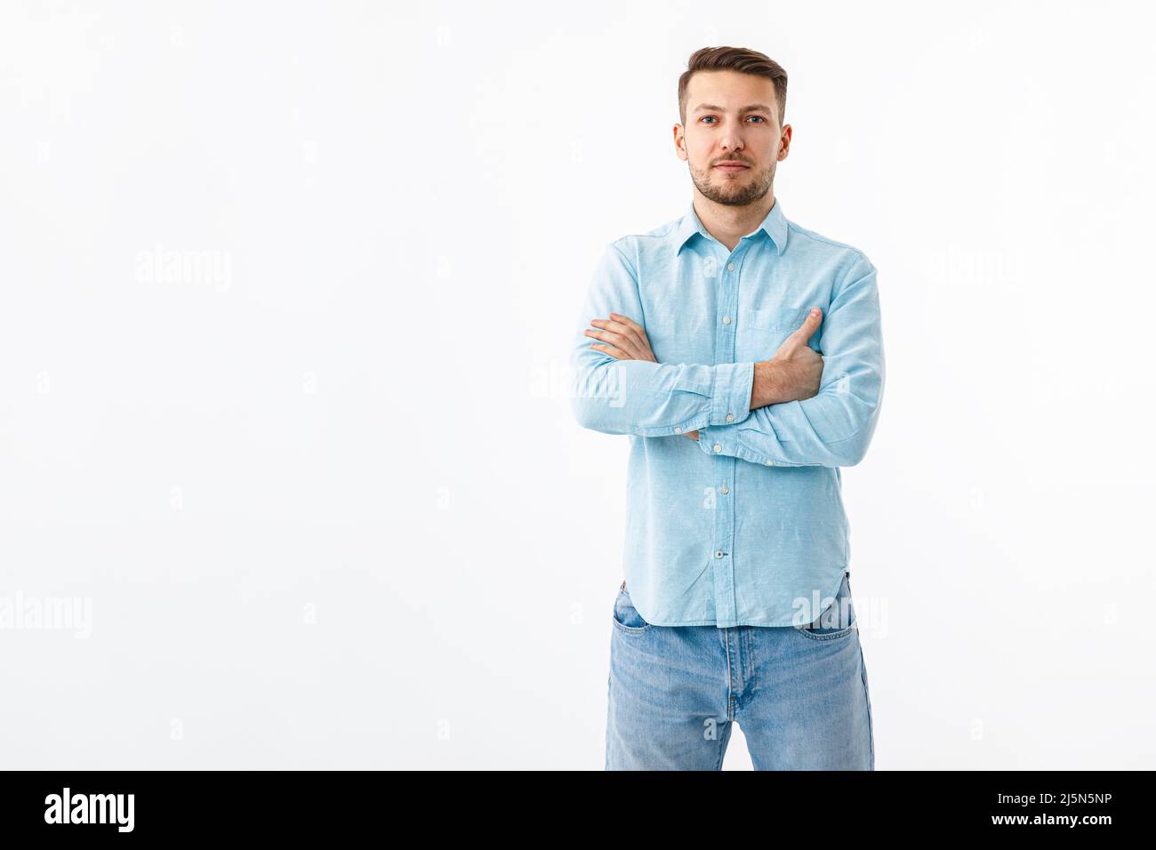 Porträt eines fröhlichen jungen Mannes in einem blauen Hemd auf weißem Hintergrund. Der Typ steht, schaut auf die Kamera und lächelt. Stockfoto