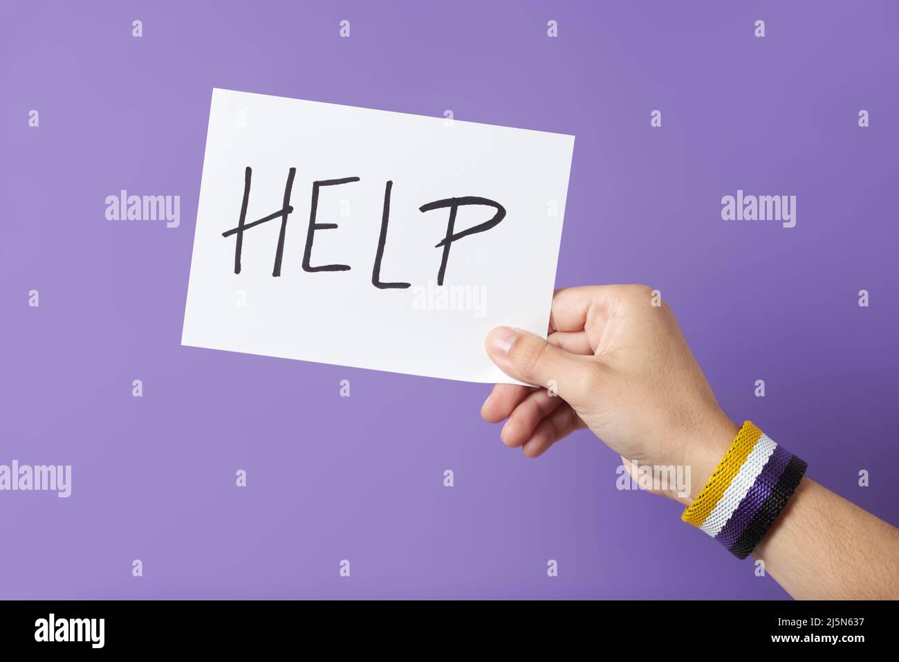 Junge Hand mit einem nicht-binären Armband mit Geschlechterflagge, das ein Stück Papier mit einer handschriftlichen Botschaft hält: Hilfe. Konzepte von Identitätsstolz, Gleichheit und Stockfoto