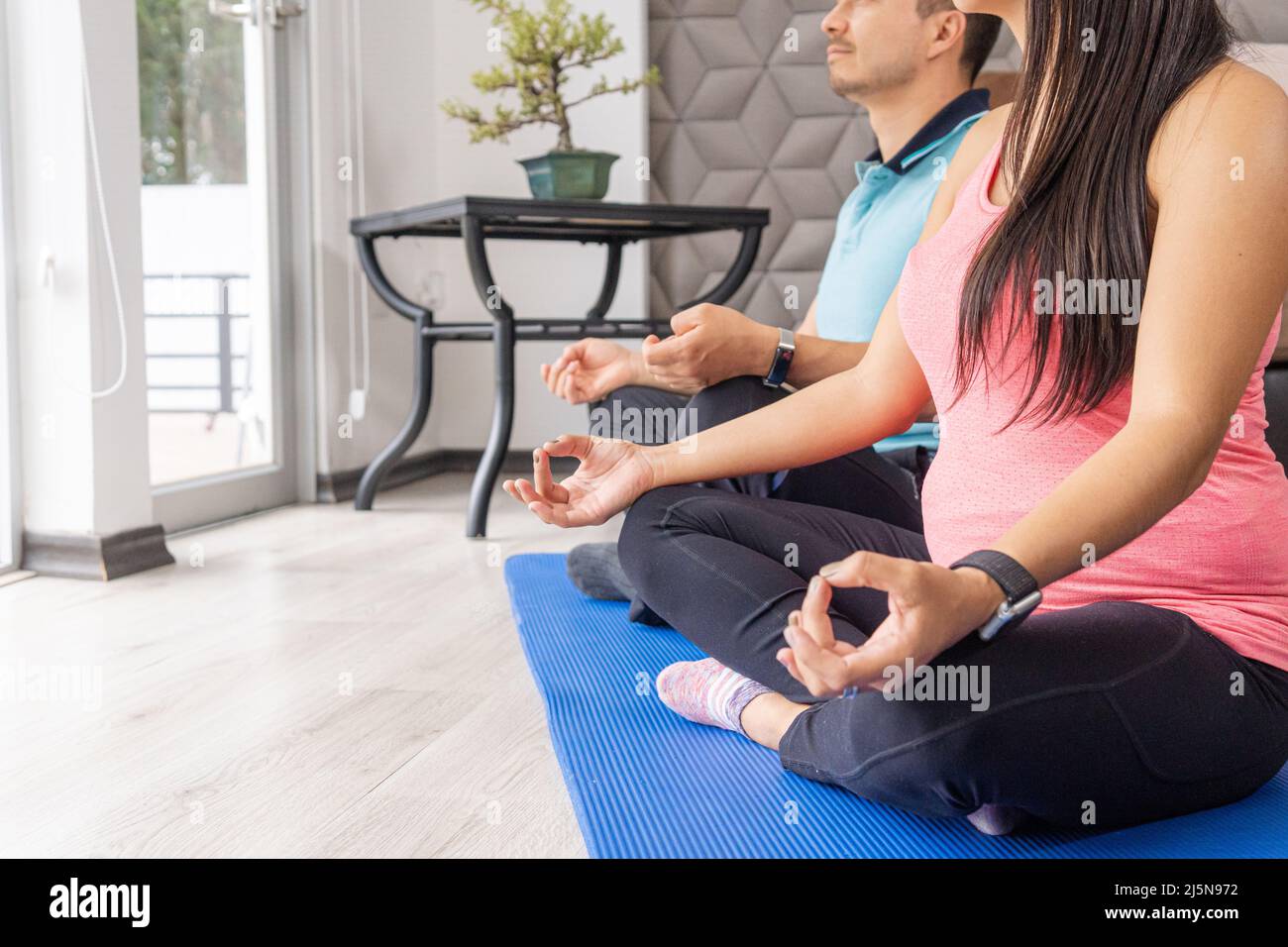 Nahaufnahme eines unverkennbaren Schwangeren- und Männerpaares, das im Wohnzimmer zu Hause Yoga und Meditation praktiziert Stockfoto