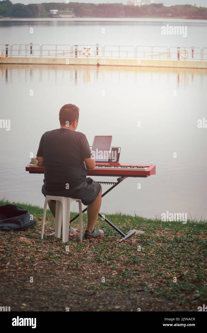 Mann spielt Klaviermusik auf Synthesizer am See. Stockfoto