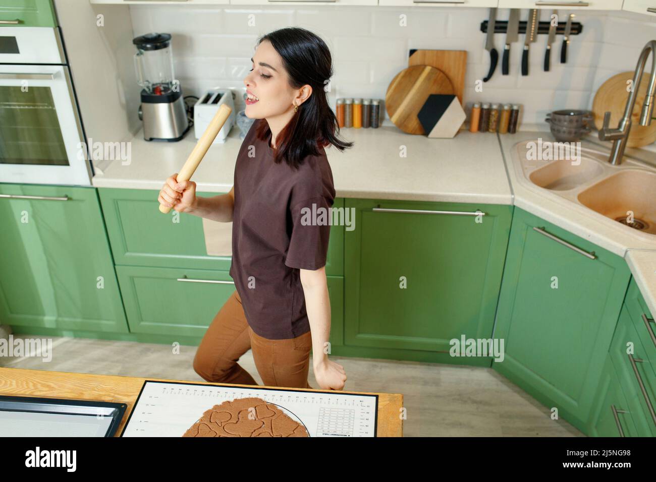 Junge glücklich fröhlich Brünette Kochen hausgemachte Kekse beim Tanzen. Stockfoto