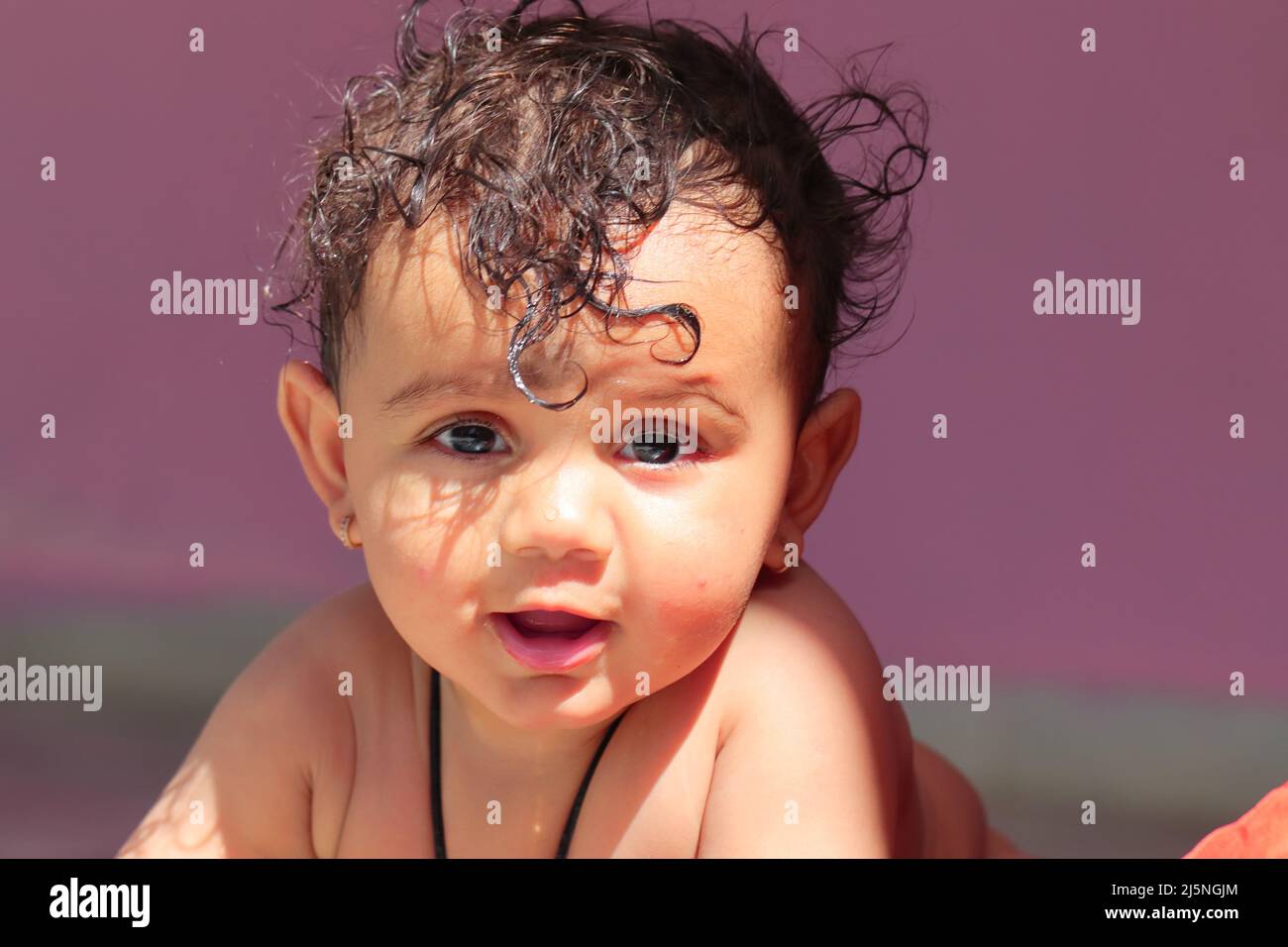 Nahaufnahme des Fotos eines kleinen, niedlichen indischen Neugeborenen, das mit natürlichem Sonnenlicht und Schatten im Gesicht und ohne Kleidung an die Kamera lächelt Stockfoto
