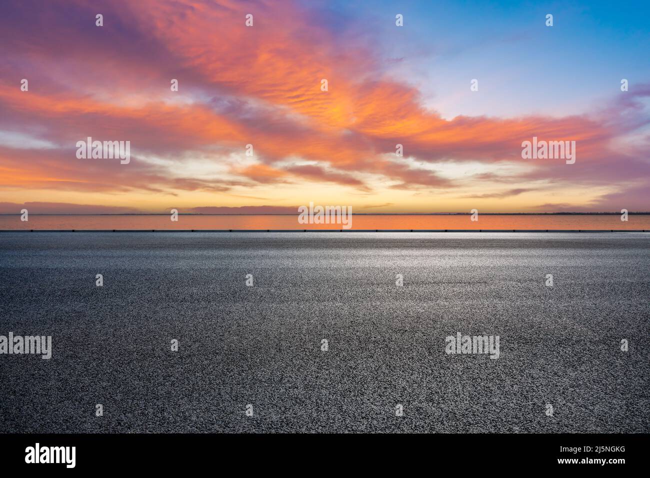 Leere Asphaltstraße und See mit wunderschönen Wolken am Himmel bei Sonnenuntergang Stockfoto