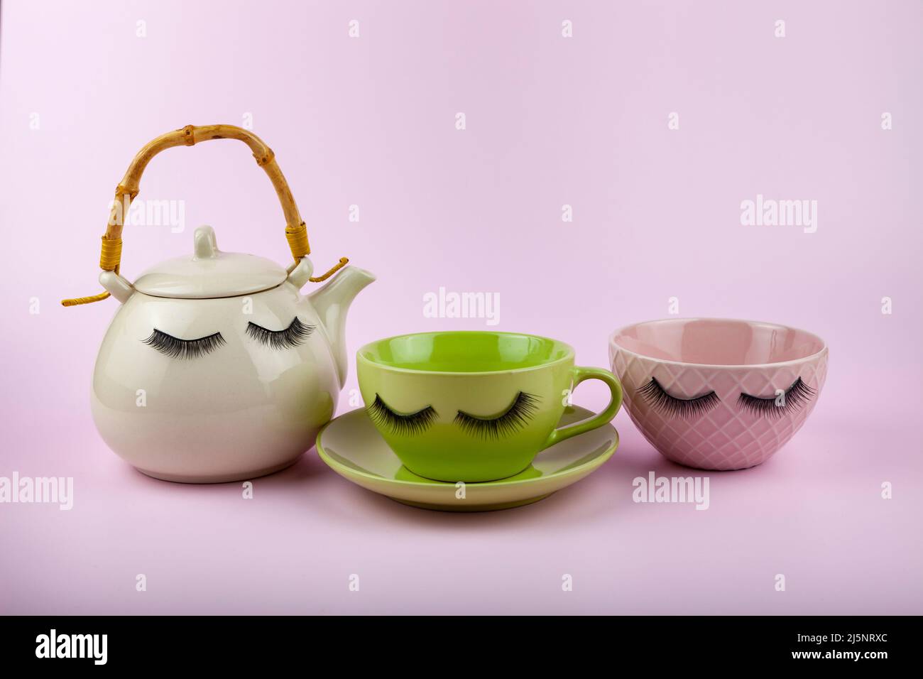 Weiße Teekannen, Tasse und Schale mit Augen auf schwarzem Hintergrund. Lustige Gerichte mit falschen Wimpern. Stockfoto