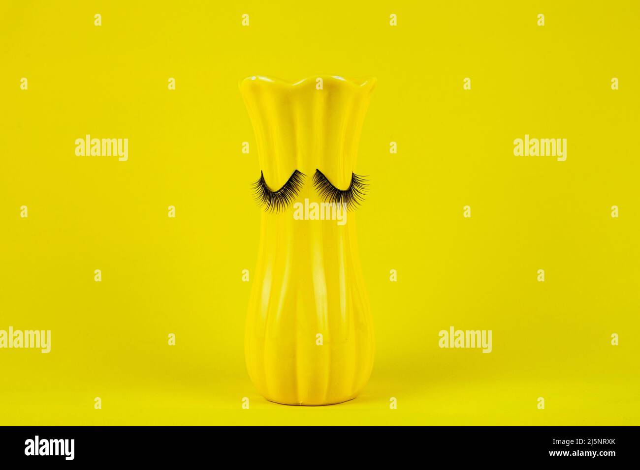 Lustige gelbe Vase mit Augen auf gelbem Hintergrund. Falsche Wimpern werden an die Vase geklebt Stockfoto
