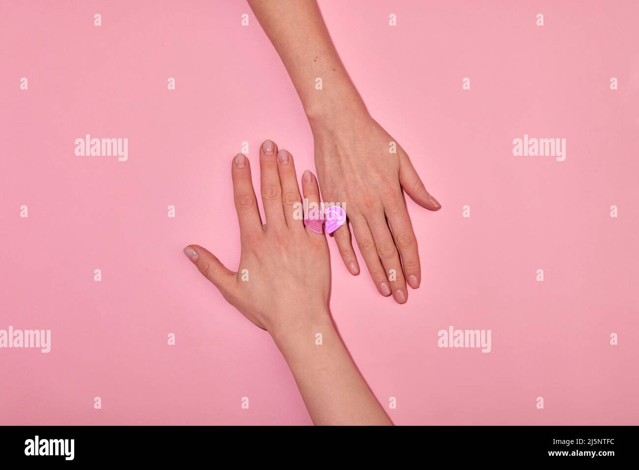 Draufsicht Hände von anonymen romantischen Paar bilden Herz mit ähnlichen Ringen an den Fingern auf rosa Hintergrund in hellen Studio Stockfoto