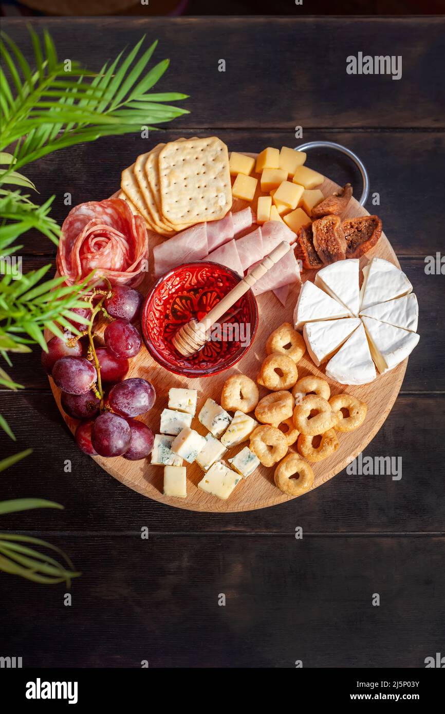 Rundes Schneidebrett mit verschiedenen Käsesorten, Wurstrosette, Schinken, Cracker, Trauben und Feigen mit Honig. Aufschnitt und Käseplatte. Draufsicht Stockfoto